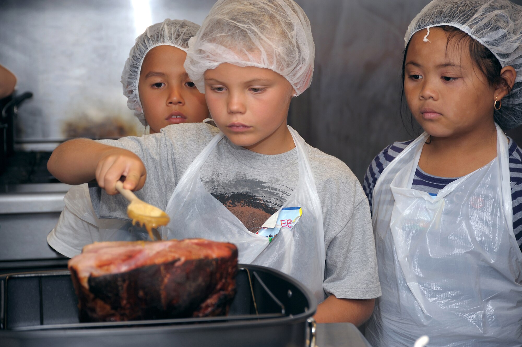 4-H culinary campers glaze a ham during the recent 4-H culinary camp. The campers learned about food preparation with the camp culminating in the eating of a meal of glazed ham, steamed snap peas and baked sweet potatoes prepared by the kids.  (Photo by Joe Juarez)