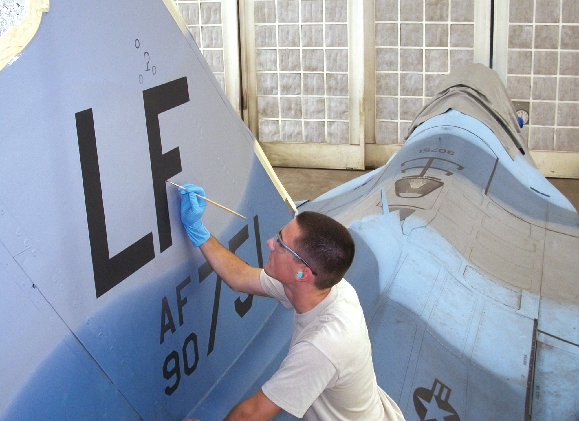 Staff Sgt. Troy Anderson, 56th Equipment Maintenance Squadron corrosion control apprentice, paints the letters "LF" for Luke Field on the vertical tail of one of the five F-16 Fighting Falcons that arrived from Nellis Air Force Base.  These five F-16 "aggressor" jets arrived with a blue camouflage paint pattern to distinguish them as aggressor aircraft during exercises.  The aircraft wil be flown at Luke with the blue camouflage pattern until they come into corrosion control to be fully repainted within the next two months. (U.S. Air Force photo/Staff Sgt. Ryan VanArtsdalen)