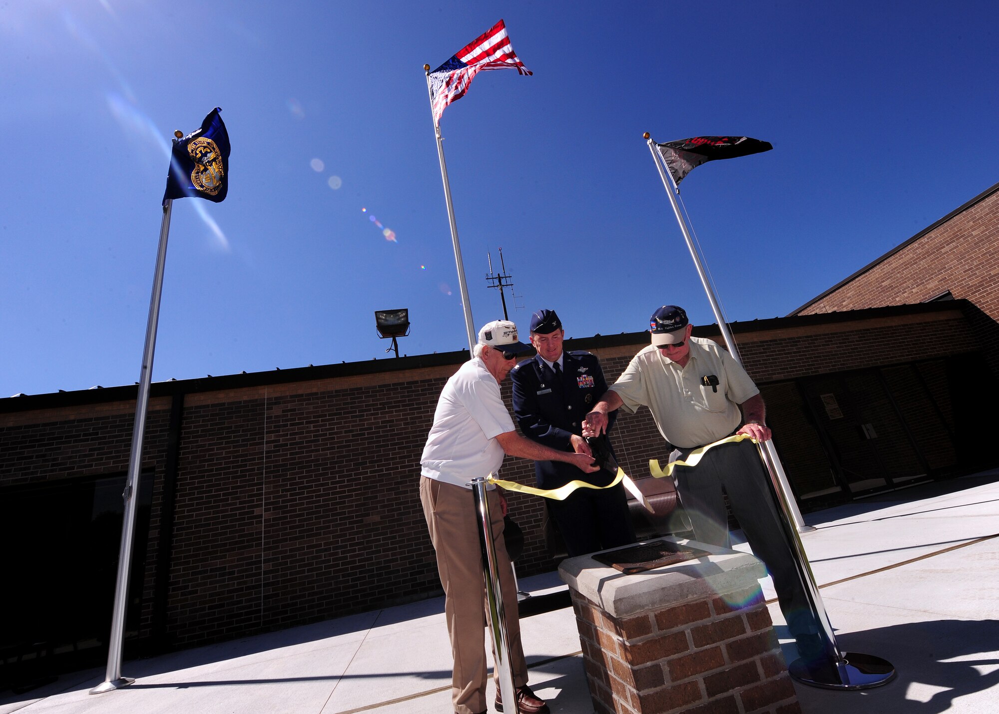 OFFUTT AIR FORCE BASE, Neb. - (From left) Don Gifford, 55th Operations Group Commander Col. John M. Hansen and George Eichhorn cut a ceremonial yellow ribbon in honor of the 55th Fighter Group during a memorial rededication Aug. 27 in front of the 55th Wing and 55th OG building.  The memorial plaque honors the heroic efforts of the fighter group. U.S. Air Force photo by Josh Plueger
