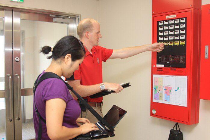 Brendan Donnelly and Mi Sun Kim Poole, Poole Fire Protection Inc. fire protection engineers, evaluate a fire alarm panel in the new Aircraft Rescue Firefighting facility here Sept. 2.  Donnelly explained the structure of the panel while Kim gathered the information on a computer attached to an engineer's "connect a desk" device.