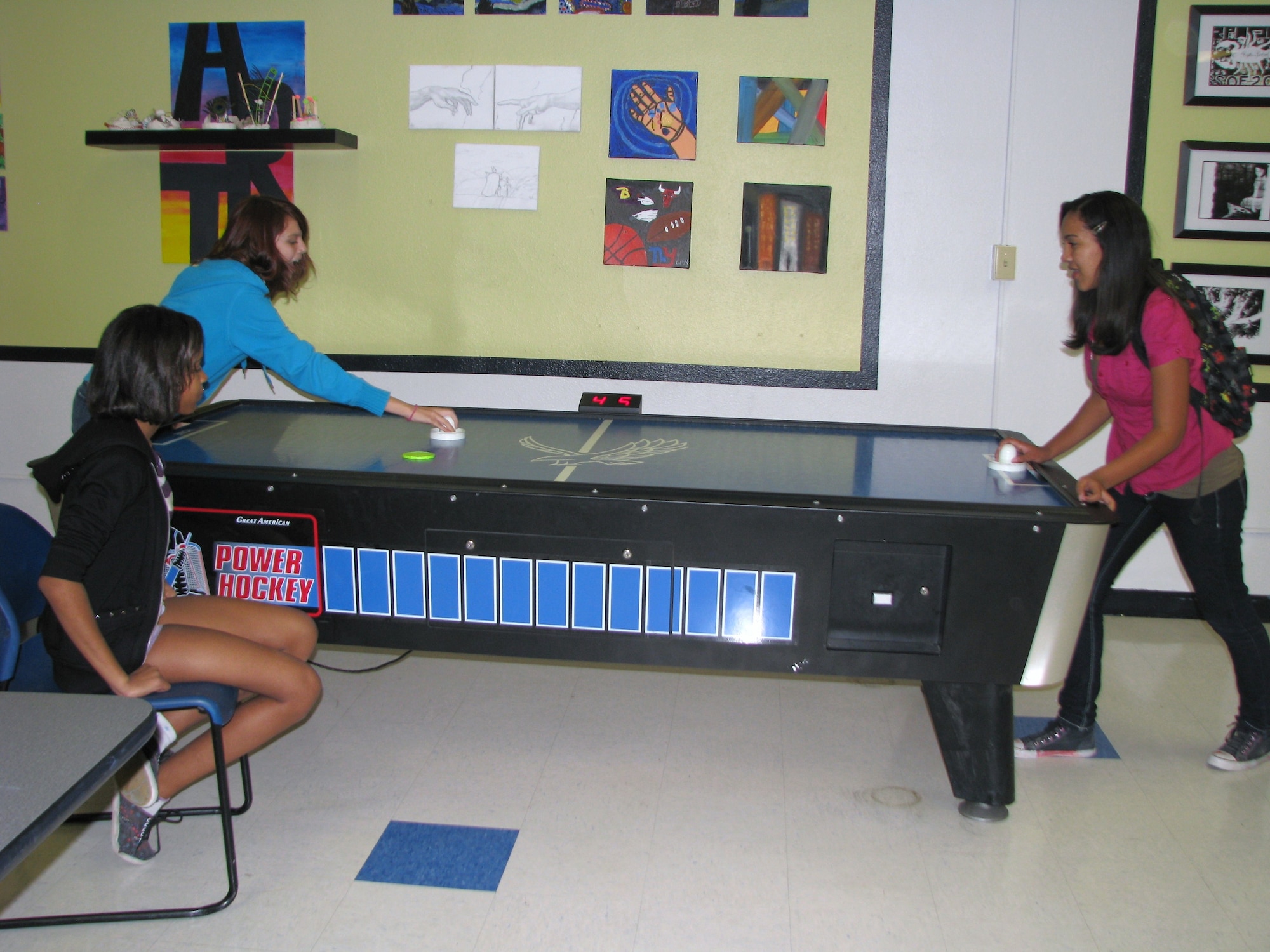Teens having fun: Desert Junior High eighth-graders enjoy a friendly after-school game of air hockey at the Edwards Teen Center while waiting for their parents. Ricara Daniels (seated) waits to challenge the winner. Players Tabitha Stankewitz, left, and Tiana Amos battle for the high score. (Air Force photo by Diane Betzler)