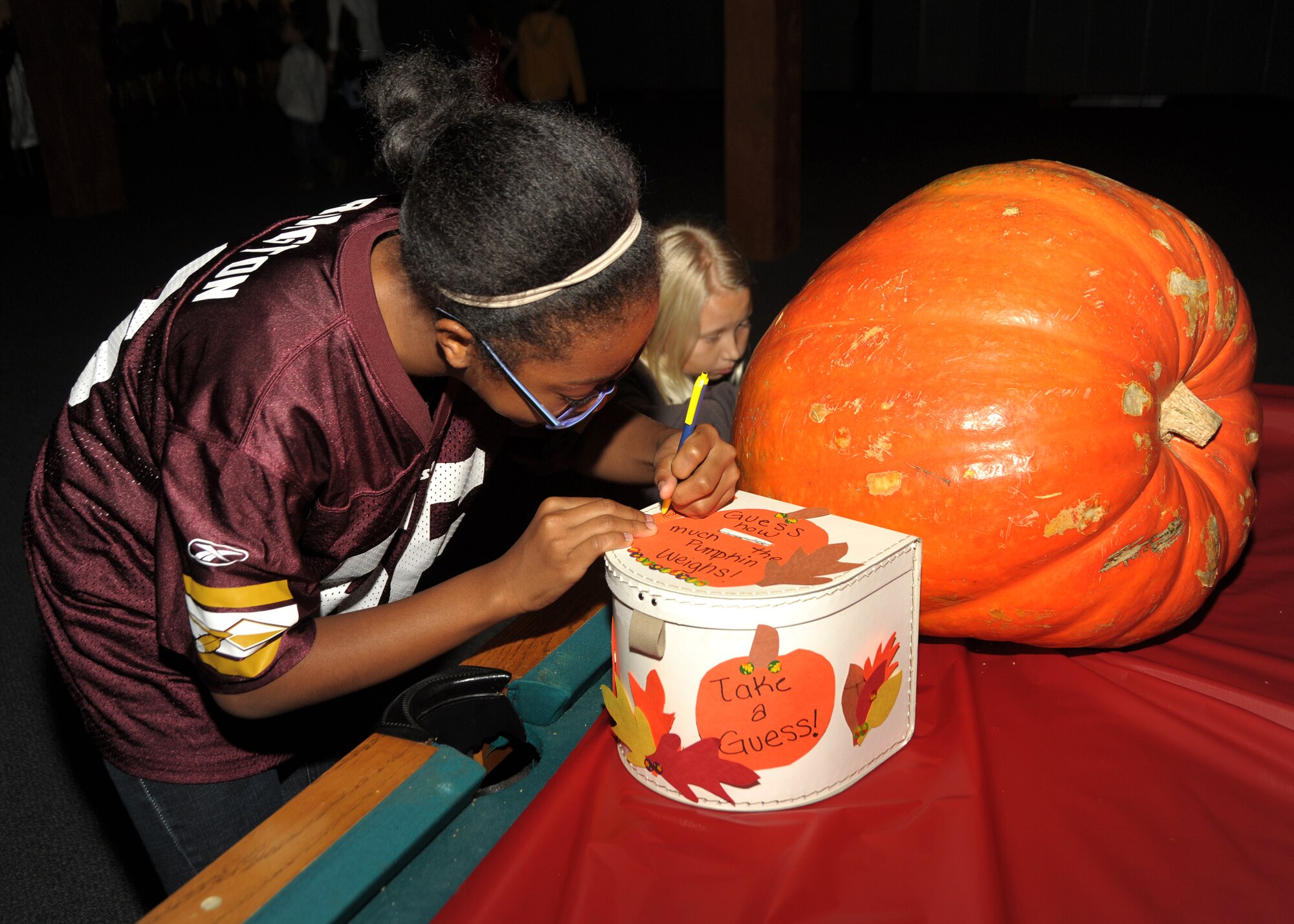 Aysia Smith takes a guess at the weight of the great pumpkin at the Family Feast Pot Luck, Nov. 18.  Los Angeles Air Force Base, 61st Force Support Squadron and Youth Programs Office hosted the event to kick off the Thanksgiving holiday and provided ham and turkey to the many side dishes brought by family members. (Photo by Joe Juarez) 