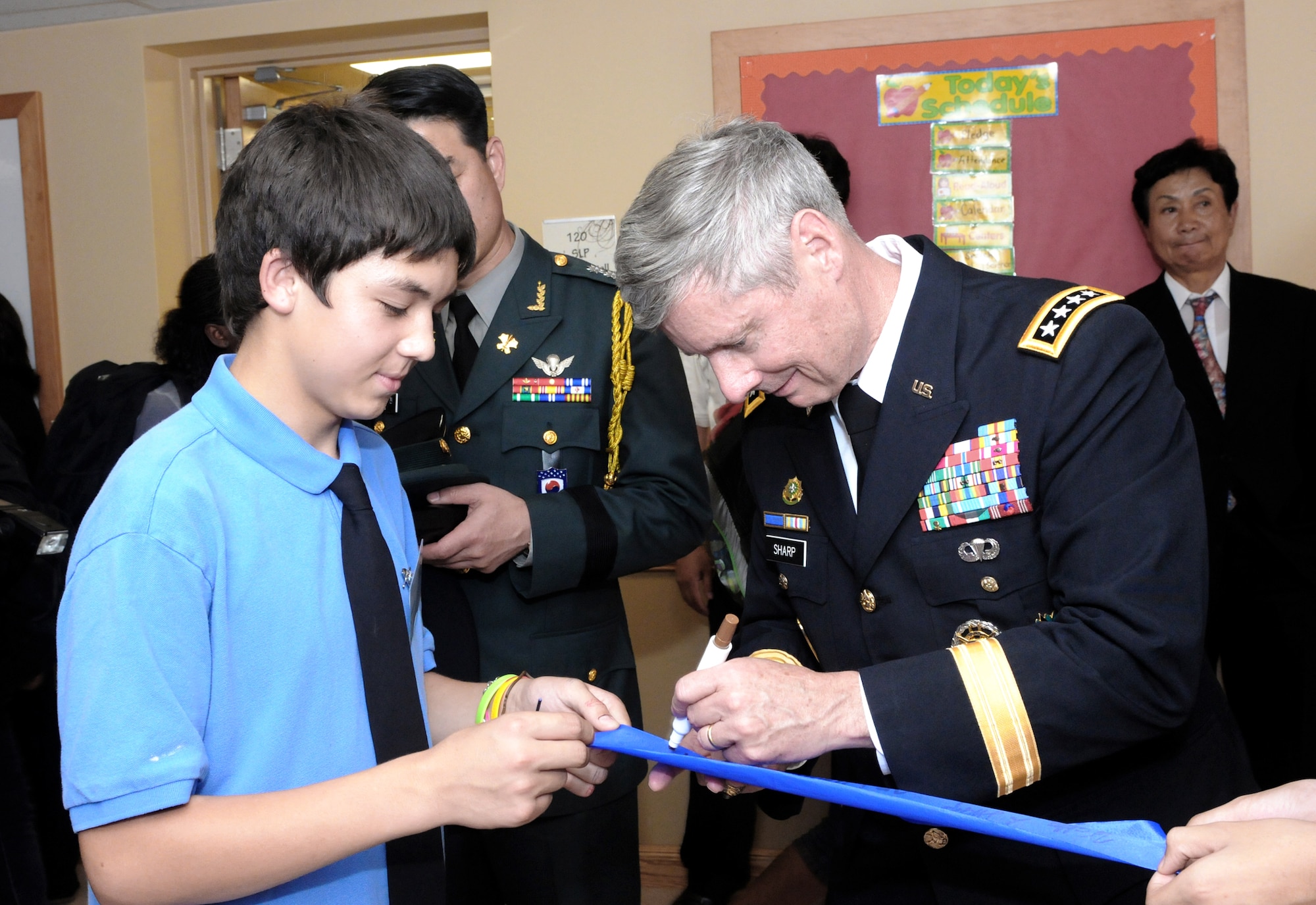 Army Gen. Walter L. Sharp chats with a student as he signs the ribbon he cut during the official opening of the new Casey Elementary School Sept. 15, 2010, at Camp Casey, South Korea. General Sharp is the commander of U.S. Forces Korea. (Courtesy photo/Yu Hu Son) 