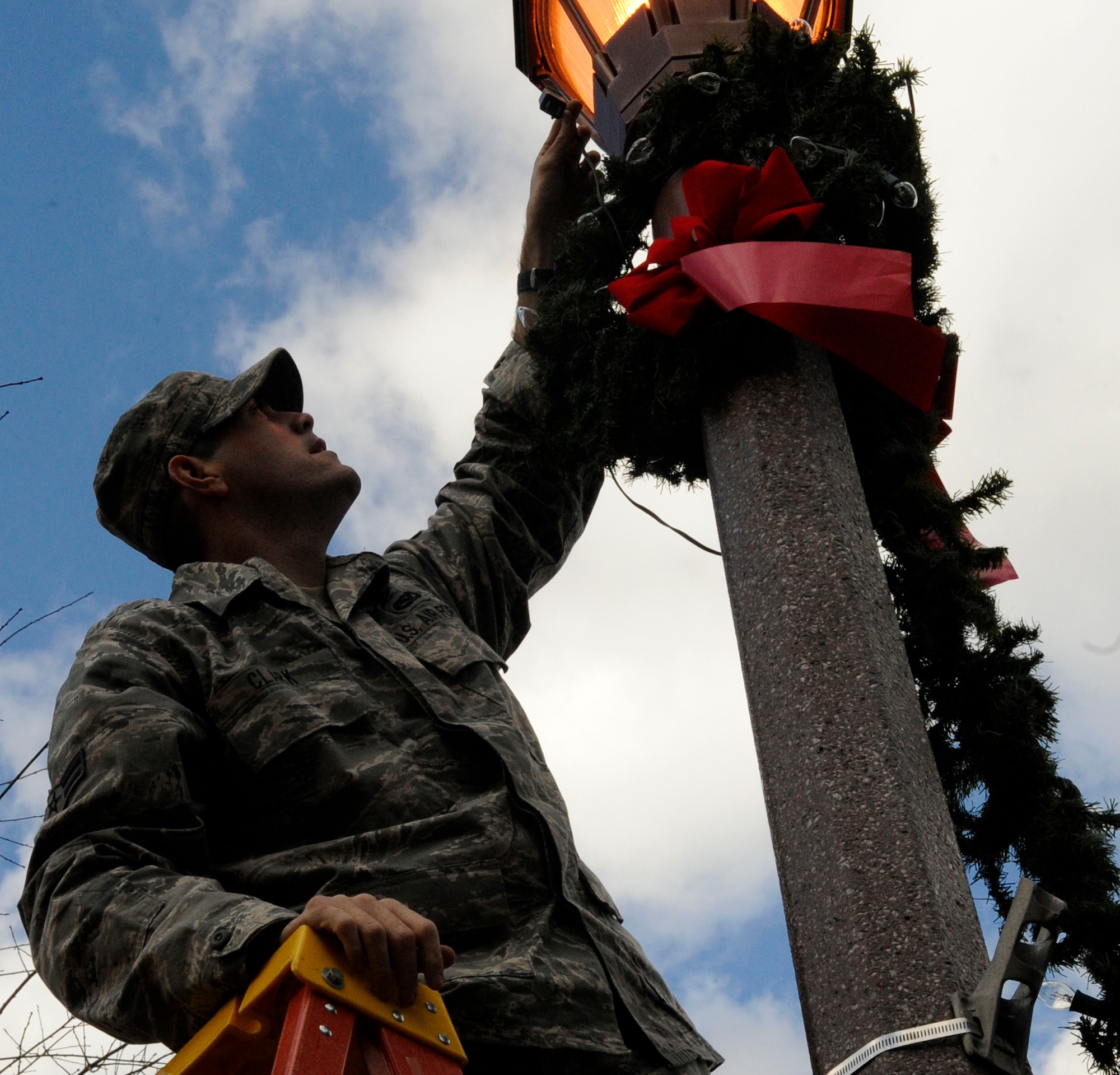 LANGLEY AIR FORCE BASE, Va.—Airman 1st Class Jared Clark, 633d Civil Engineer Squadron electrical systems apprentice, adjusts a holiday wreath wrapped around a light pole Dec. 1. The Civil Engineer Squadron went around the installation decorating to prepare the base for the holiday season. (U.S. Air Force photo/Staff Sgt. Dana Hill)(RELEASED)
