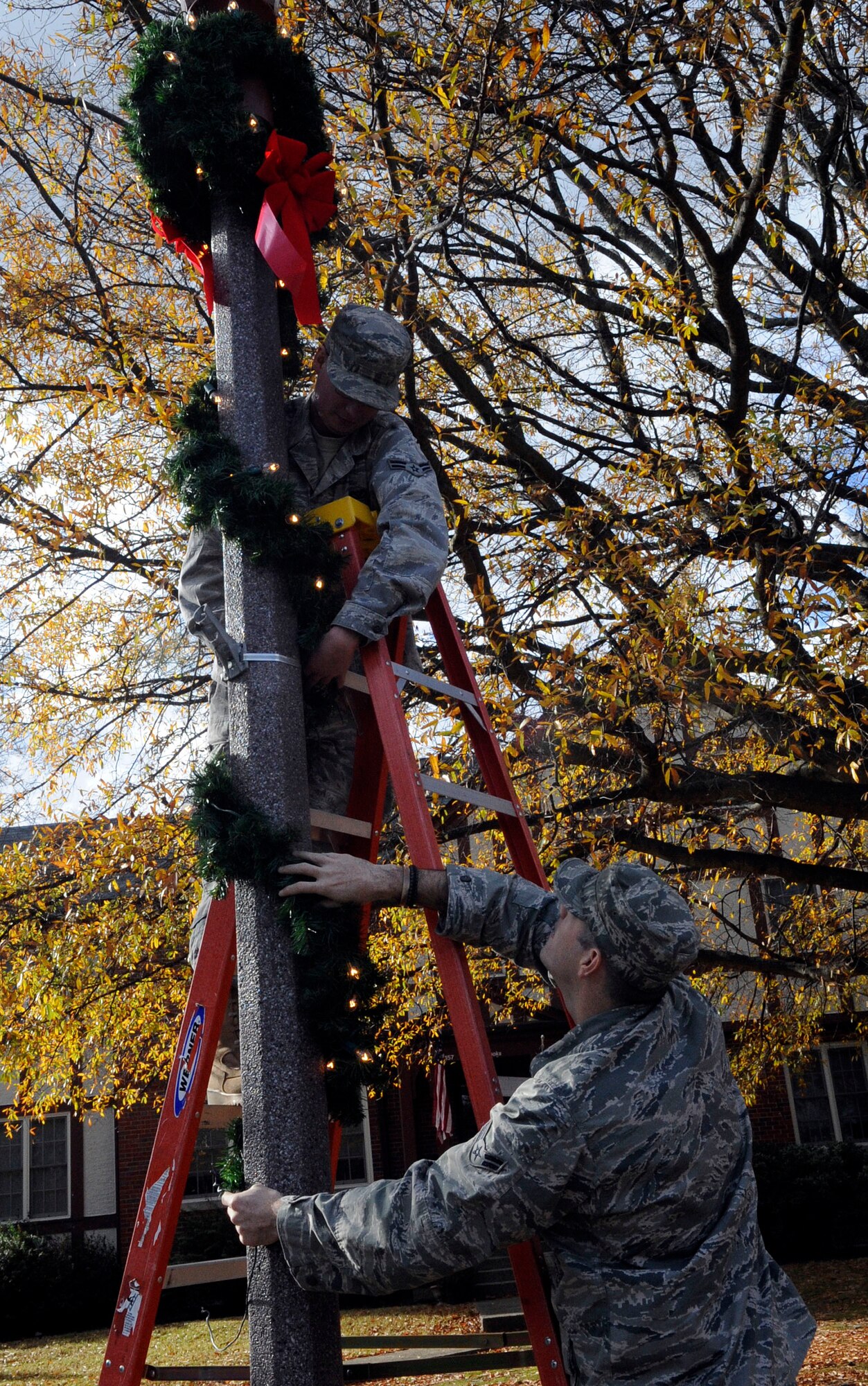 LANGLEY AIR FORCE BASE, Va.—Airman 1st Class Jared Clark, 633d Civil Engineer Squadron electrical systems apprentice, holds pieces of a wreath while Airman 1st Class Nathanel Witt, also an electrical systems apprentice with the 633d Civil Engineer Squadron, wraps the wreath around a light pole Dec. 1. The Civil Engineer Squadron went around the installation decorating to prepare the base for the holiday season. (U.S. Air Force photo/Staff Sgt. Dana Hill)(RELEASED)