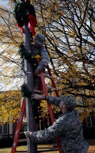 LANGLEY AIR FORCE BASE, Va.—Airman 1st Class Jared Clark, 633d Civil Engineer Squadron electrical systems apprentice, holds pieces of a wreath while Airman 1st Class Nathanel Witt, also an electrical systems apprentice with the 633d Civil Engineer Squadron, wraps the wreath around a light pole Dec. 1. The Civil Engineer Squadron went around the installation decorating to prepare the base for the holiday season. (U.S. Air Force photo/Staff Sgt. Dana Hill)(RELEASED)