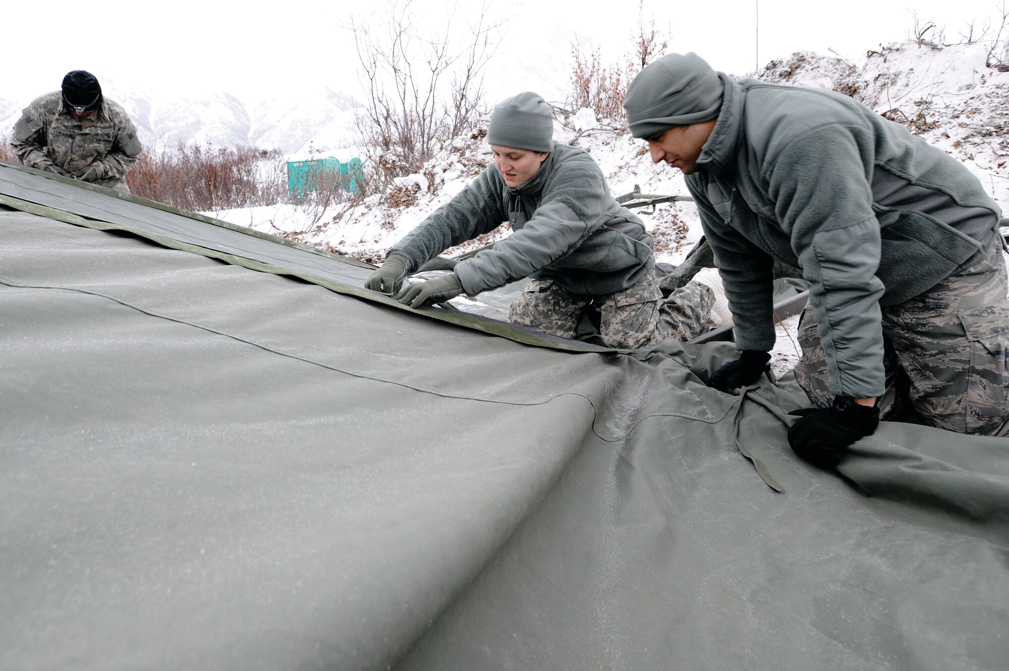 FORWARD OPERATING BASE GILLASPIE, Alaska -- Airman 1st Class Victoria Reinhart and Air Force Staff Sgt. Andrew Hernandez, both bio-environmental technicians with the 673d Aerospace Medical Squadron, secure the tarp to the outer frame of a tent at Site Raptro, Nov. 22. The tent would become the Medical Clinic at Foward Operating Base Gillaspie, providing support to 175 service members. (Photo by Air Force Staff Sgt. Joshua Garcia/JBER PAO)