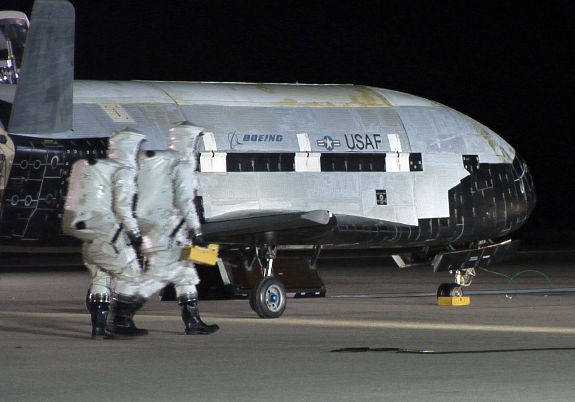 The X-37B sits on the Vandenberg Air Force base runway during post-landing operations Dec. 3. Personnel in SCAPE (Self-contained atmospheric protective ensemble) suits conduct initial checks on the vehicle and ensuring the area is safe. (U.S. Air Force photo/ Michael Stonecypher)