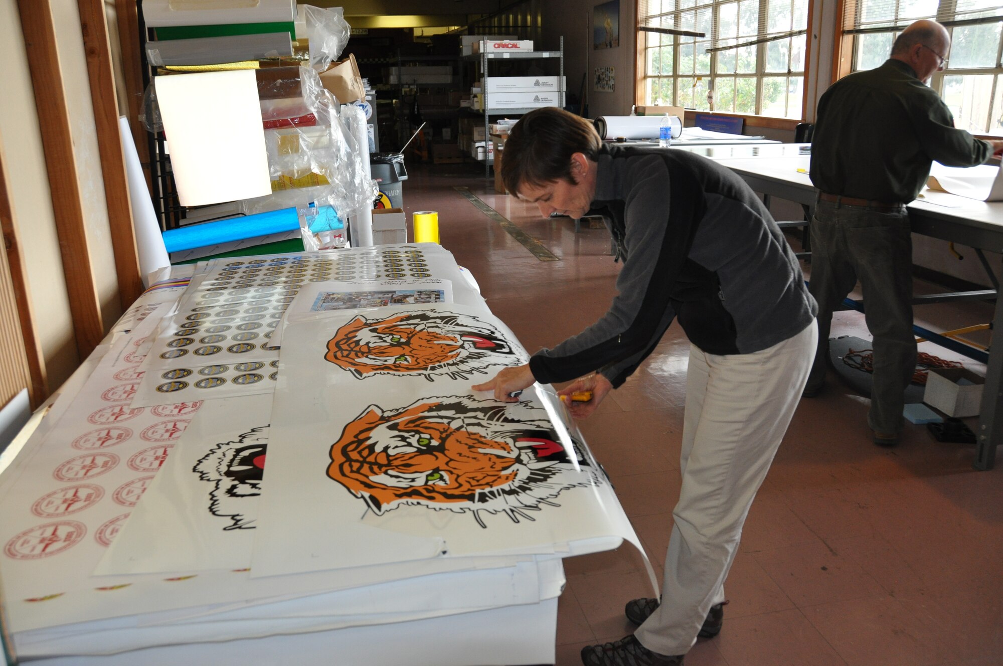 Katherine Kruczek, DLA Document Services graphic artist, "weeding" decals for a HSL-43 Battle Cats helicopter Dec. 1. Later that day, Kruczek prepared an order of 100,000 promotional decals for the Centennial of Naval Avaiation yearlong celebration.( U.S. Air Force photo/Airman 1st Class Michael Battles)