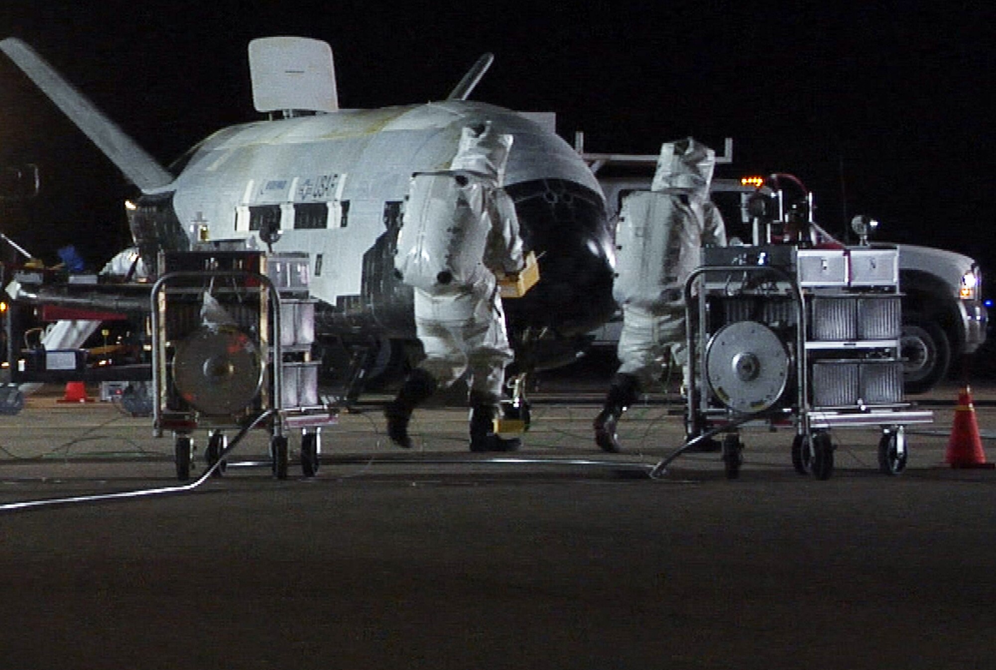 The X-37B Orbital Test Vehicle sits on the runway at Vandenberg Air Force Base, Calif., Dec. 3, 2010, during post-landing operations. Personnel in self-contained atmospheric protective ensemble suits are conducting initial checks on the vehicle and ensuring the area is safe.  The X-37B launched April 22 from Cape Canaveral, Fla., allowing teams to conduct on-orbit experiments for more than 220 days during this first mission.  (U.S. Air Force photo) 
