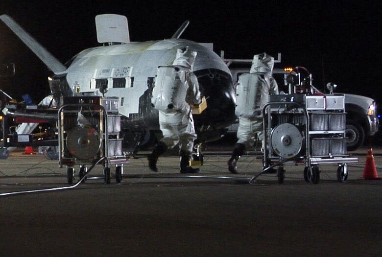 The X-37B Orbital Test Vehicle sits on the runway at Vandenberg Air Force Base, Calif., Dec. 3, 2010, during post-landing operations. Personnel in self-contained atmospheric protective ensemble suits are conducting initial checks on the vehicle and ensuring the area is safe.  The X-37B launched April 22 from Cape Canaveral, Fla., allowing teams to conduct on-orbit experiments for more than 220 days during this first mission.  (U.S. Air Force photo) 
