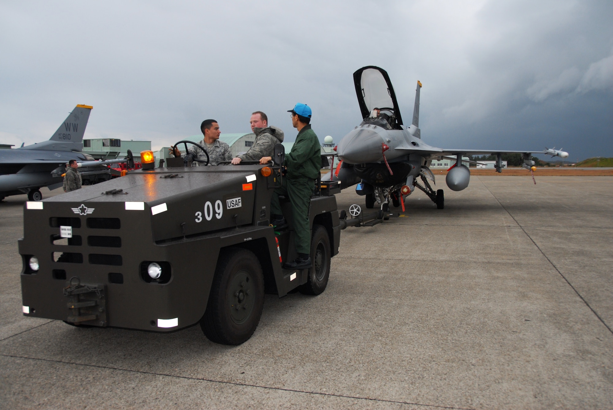 U.S. Air Force Airman 1st Class Hector Arrayo, left, and Staff Sgt. Robert Ensley, 35th Aircraft Maintenance Squadron crew chiefs, operate a Japanese towing vehicle, towing an F-16 Fighting Falcons to a Komatsu Air Self-Defense Force Base hangar Dec. 3, 2010. The hangar stores aircraft during inclement weather to prevent damages to the aircraft caused by lightning, wind or hail. (U.S. Air Force photo by 1st Lt. Cammie Quinn/ Released)