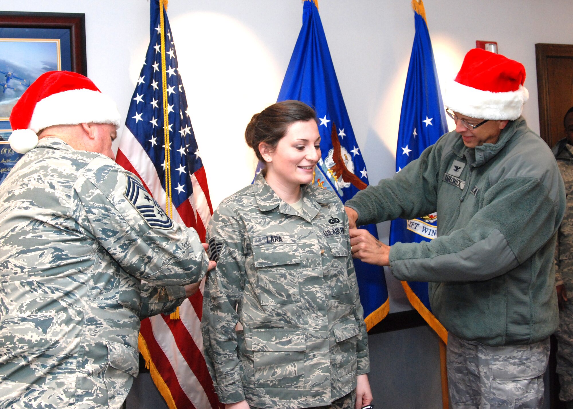 In a holiday festive spirit, 94th Airlift Wing Command Chief Master Sgt. John Anderson and Col. Timothy Tarchick, 94th AW commander, give newly promoted Tech. Sgt. Viki Lara, command post technician, the traditional tap on the arms, signifying her new rank Dec. 4.  (U.S. Air Force photo/Master Sgt. Stan Coleman)