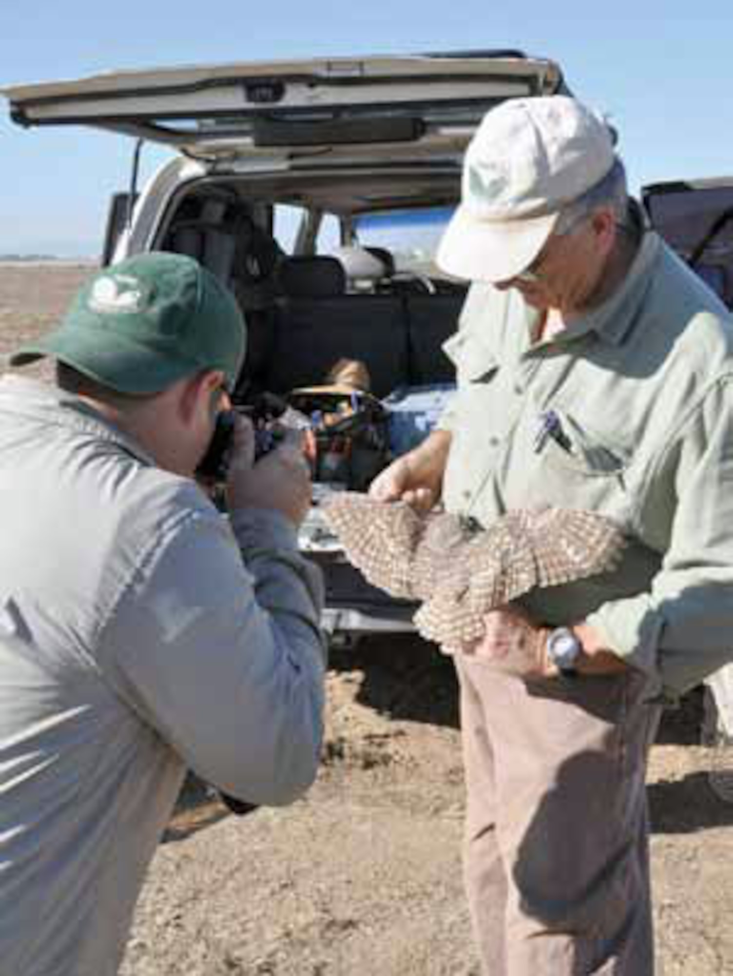 Dr. Jeffrey Lincer holds a burrowing owl still while Daniel Palmer photographs the owl’s feathers for research purposes. (U.S. Air Force photo by Megan Just)