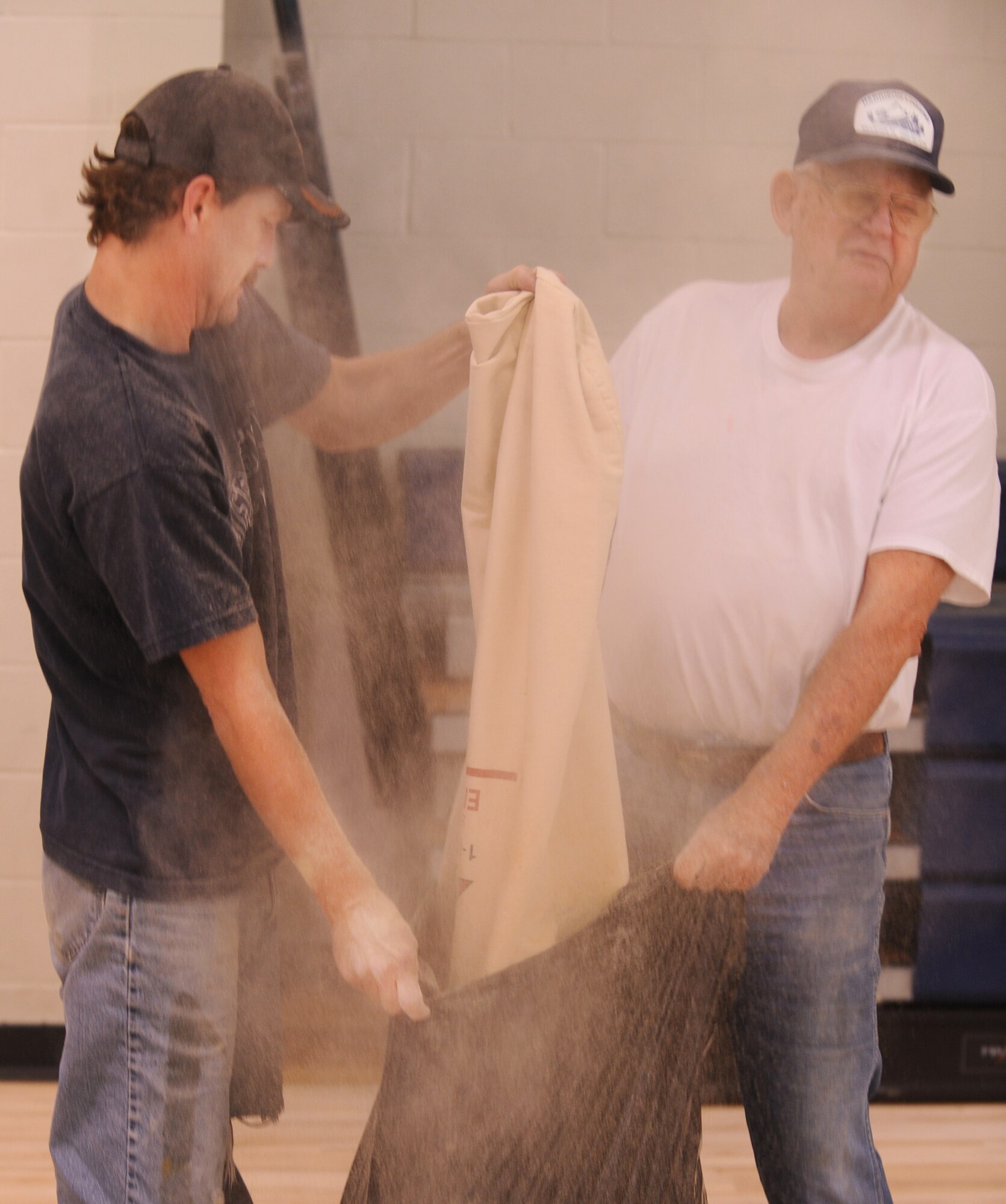 MOODY AIR FORCE BASE, Ga. -- Mike Webb (left) and Andy Reid, contracted workers, empty a bag of dust from a riding sander inside the Freedom I Fitness Center Dec. 1. Similar to a Vacuum, riding sanders collect the powder and dust created when sanding wax from floors into bags. (U.S. Air Force Photo/Airman 1st Class Douglas Ellis)(RELEASED)