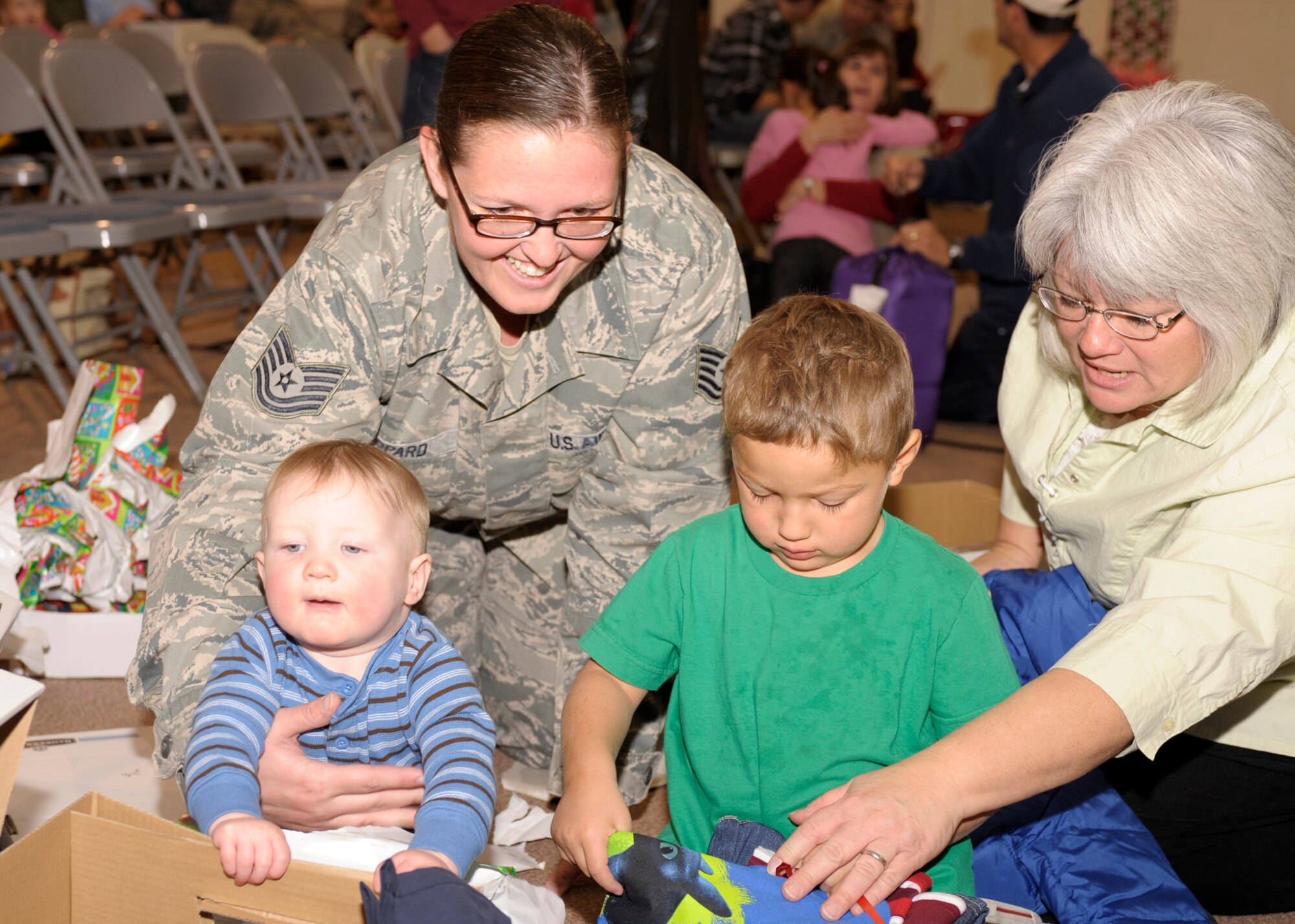 Tech. Sgt. Stephanie Leopard, 27th Special Operations Medical Support Squadron, her son Jake, and April Barnhart watch as Ricky Padilla eagerly opens his gifts at the 7th Annual Blue Angels Christian Children's Home Holiday Event on Dec. 5. The Blue Angels donated gifts to the 73 children who live at the home, and then attended the Christmas party held in the organizations gymnasium. (U.S. Air Force Photo by Airman Ericka Engblom)