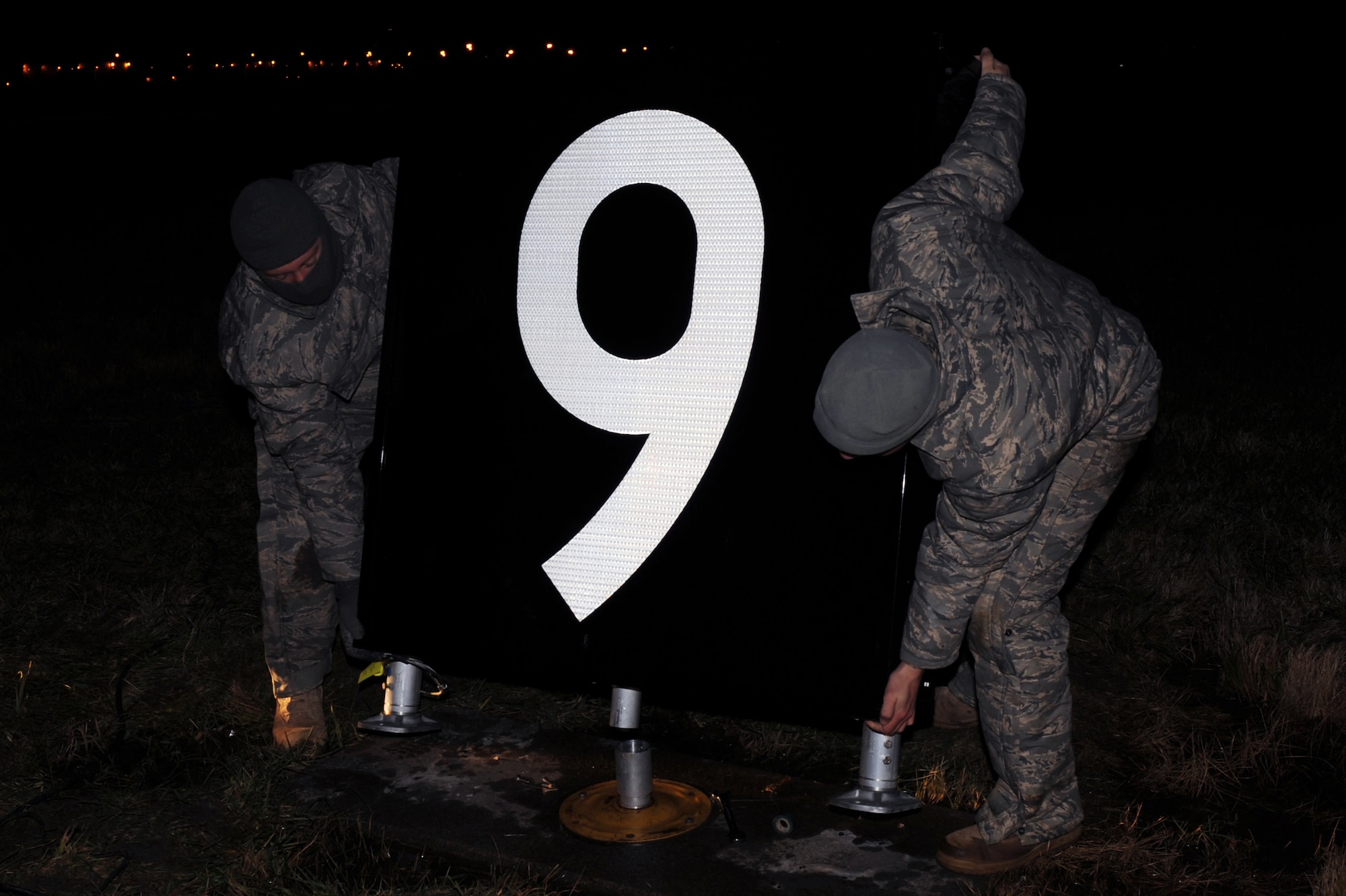 WHITEMAN AIR FORCE BASE, Mo. -- Airman 1st Class Raymond Reidenbach and Airman 1st Class Corey Logsdon, 509th Civil Engineer Squadron electrician, are setting the new light-emitting diode distance-remaining marker in place next to the runway. The LED fixtures are designed to cut energy costs by 70 percent. (U.S. Air Force photo/Staff Sgt. Jason Huddleston) (Released)