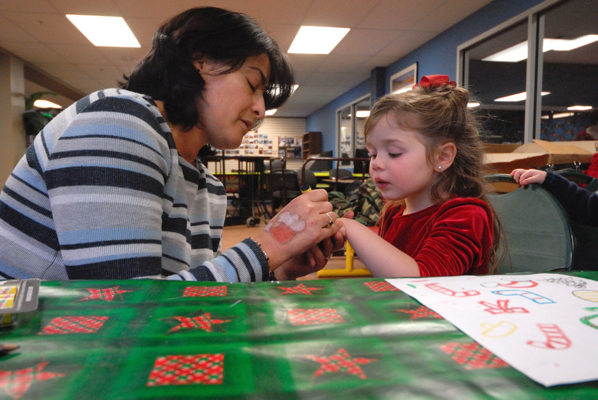 Maria Hudson, Richardson Child Development Center, applies hand paint to 4-year-old Gabriella Thibodeau, daughter of Air Force Staff Sgt. Danielle Gagne-Thibodeau, 673d Medical Group, during the Breakfast with Santa at the Arctic Oasis Community Center, Dec. 4. (U.S. Air Force photo/Steven White)