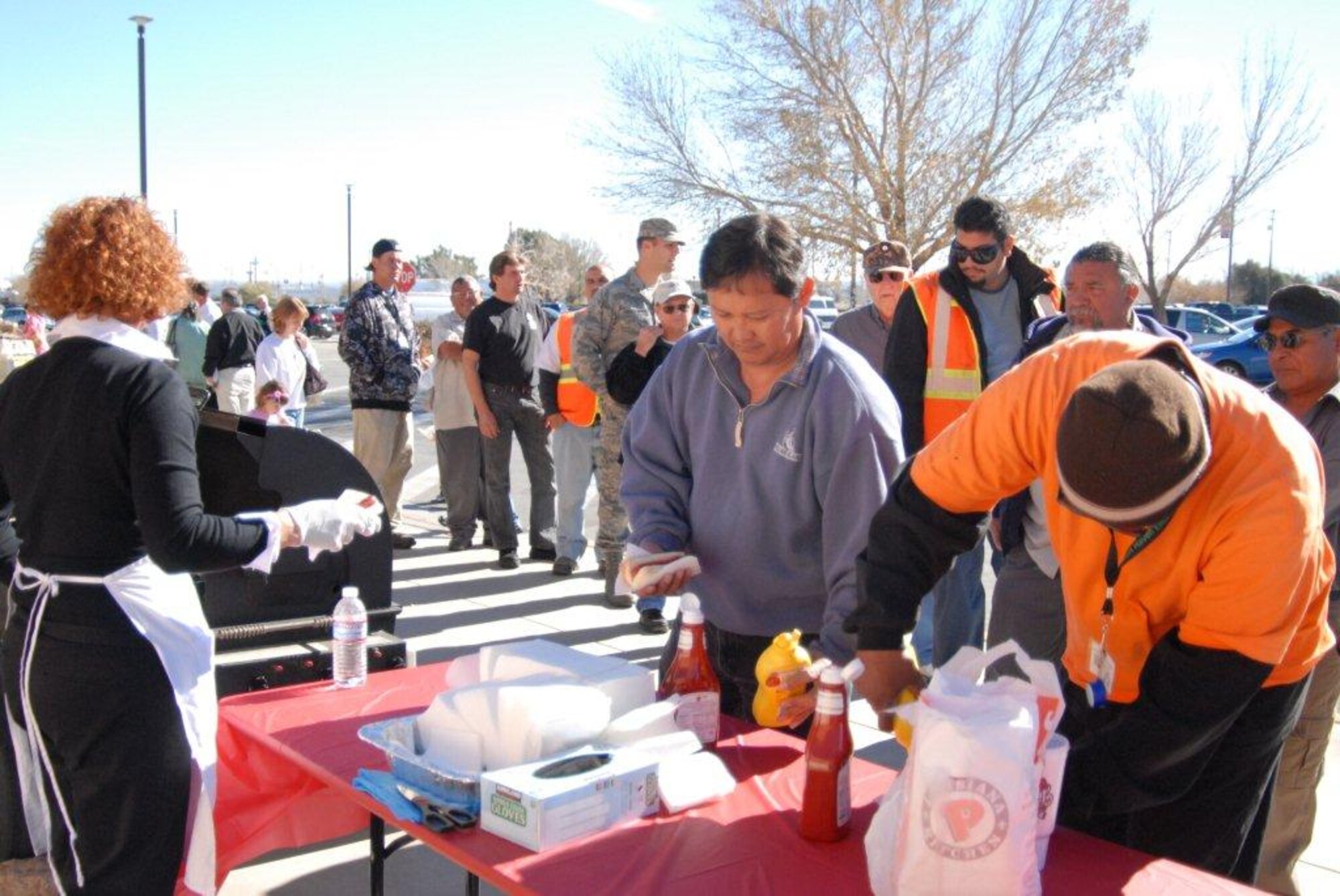 An Oscar Mayer Wienermobile staff member hands out free hot dogs as Edwards community members load up their links with condiments at a hot dog stand set up in front of the Edwards commissary Dec. 1. The Wienermobile visited the  base and the staff, known as Hotdoggers, spent the day handing out free hot dogs and stickers. (Air Force photo by Kenji Thuloweit)