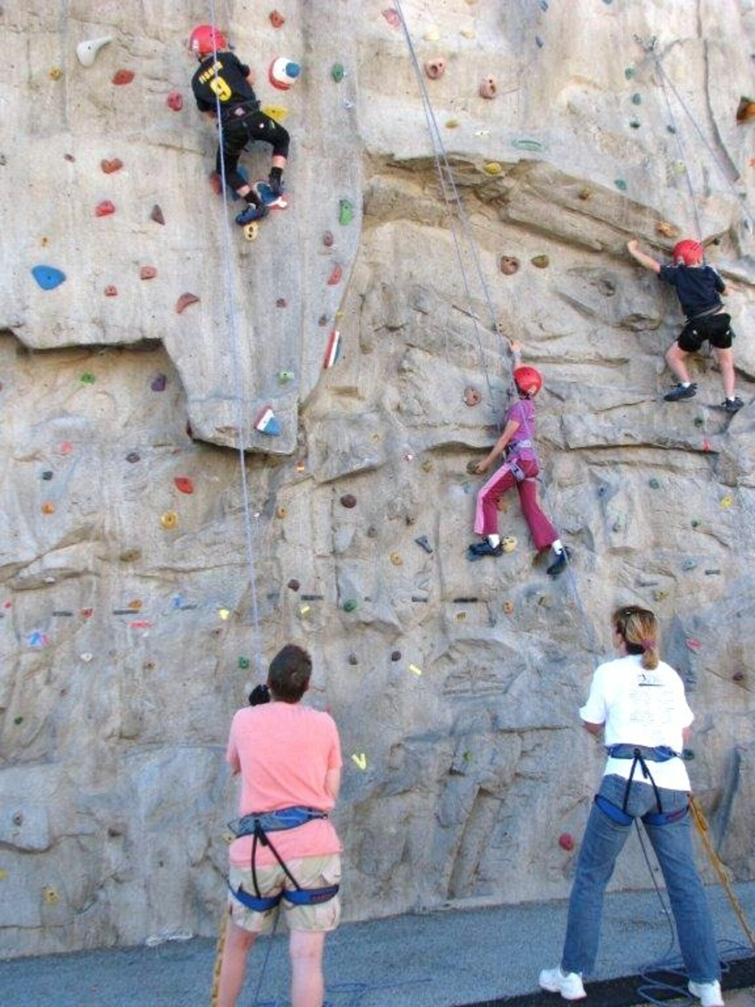 Home-schooled children meet state physical education requirements at the Oasis Aquatic Center while having fun climbing a 30-foot-high wall. Guiding the children through the exercise are belay-certified parents, Beth Gray (pink shirt) and CeCe Fisher (white t-shirt). Climbers are: (top left) 8-year-old Damian Fisher; Erin Gray, 10; and Will Fisher, 6. (Air Force photo by Diane Betzler)
