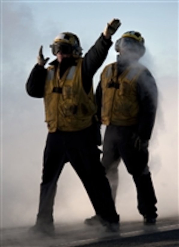 U.S. Navy Petty Officer 2nd Class Jathan Lane (left), an aircraft director assigned to V-1 Division of the air department aboard the aircraft carrier USS Carl Vinson (CVN 70), guides an aircraft onto a steam-powered catapult as Petty Officer 3rd Class David Myrtil observes under instruction while underway in the Pacific Ocean on Dec. 1, 2010.  The Carl Vinson and Carrier Air Wing 17 conducted a three-week composite training unit exercise before a deployment to the western Pacific Ocean.  