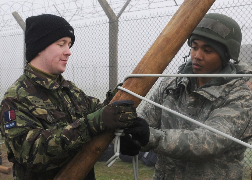RAF MARHAM, England -- Royal Air Force Senior Aircraftman Technician Martin Dovey, 31st Squadron, RAF Marham, and Senior Airman Leroy Jackson, 100th Communication Squadron, tie a bungee cord to a pine pole while building a sling shot to launch a ball at a target during Leader, Ethos and Air Power Training Day here Dec. 6, 2010. Teams were given raw materials to build a device to launch a volleyball with distance and accuracy. (U.S. Air Force photo/Senior Airman Tabitha M. Lee)  