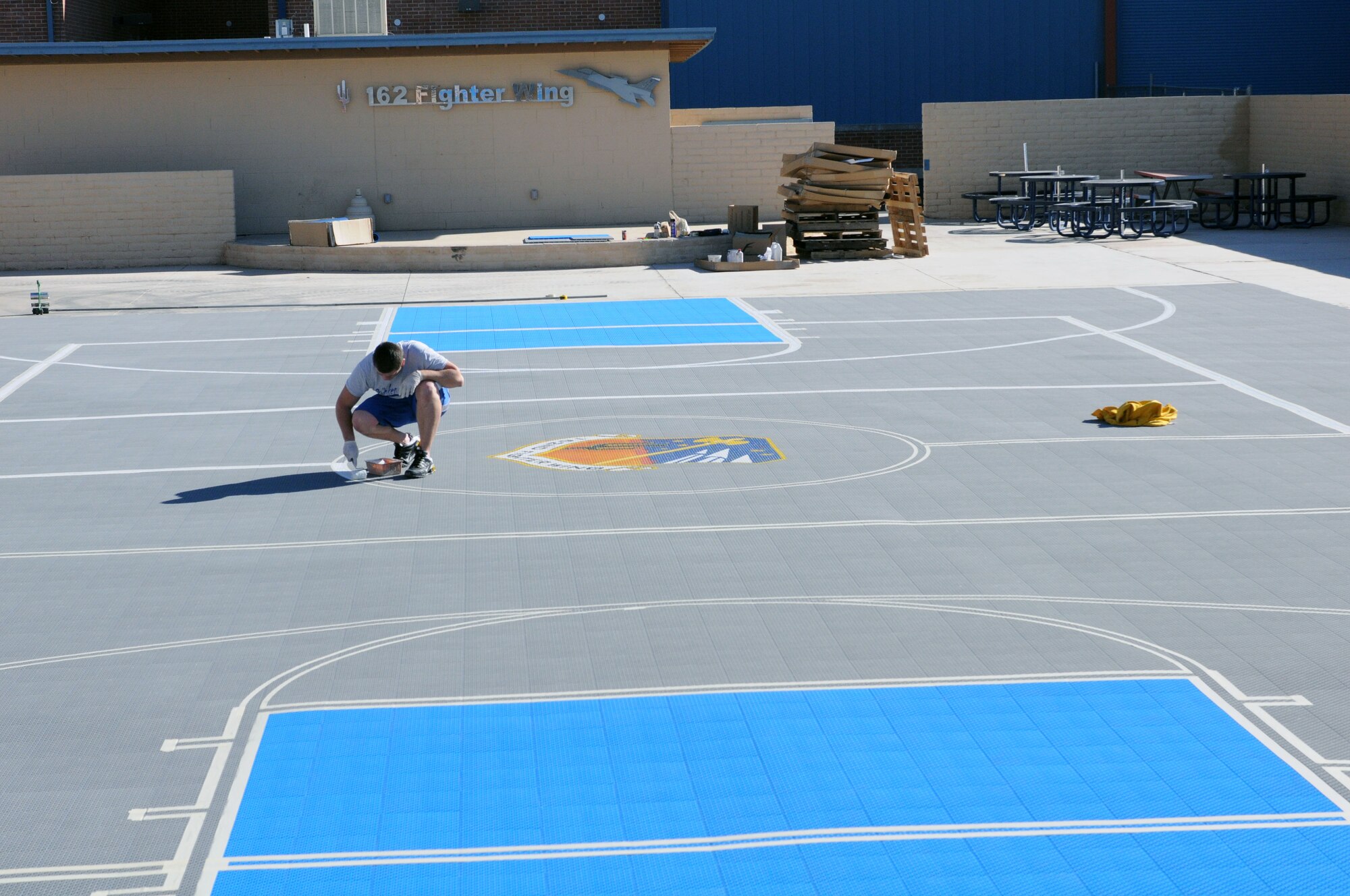 A contractor hired to install the 162nd Fighter Wing’s new basketball court at Tucson International Airport paints lines around the wing patch at center court Dec. 10. The new court behind building 15 will provide more useable space on base for sporting and social events. (Air Force photo/Maj. Gabe Johnson)