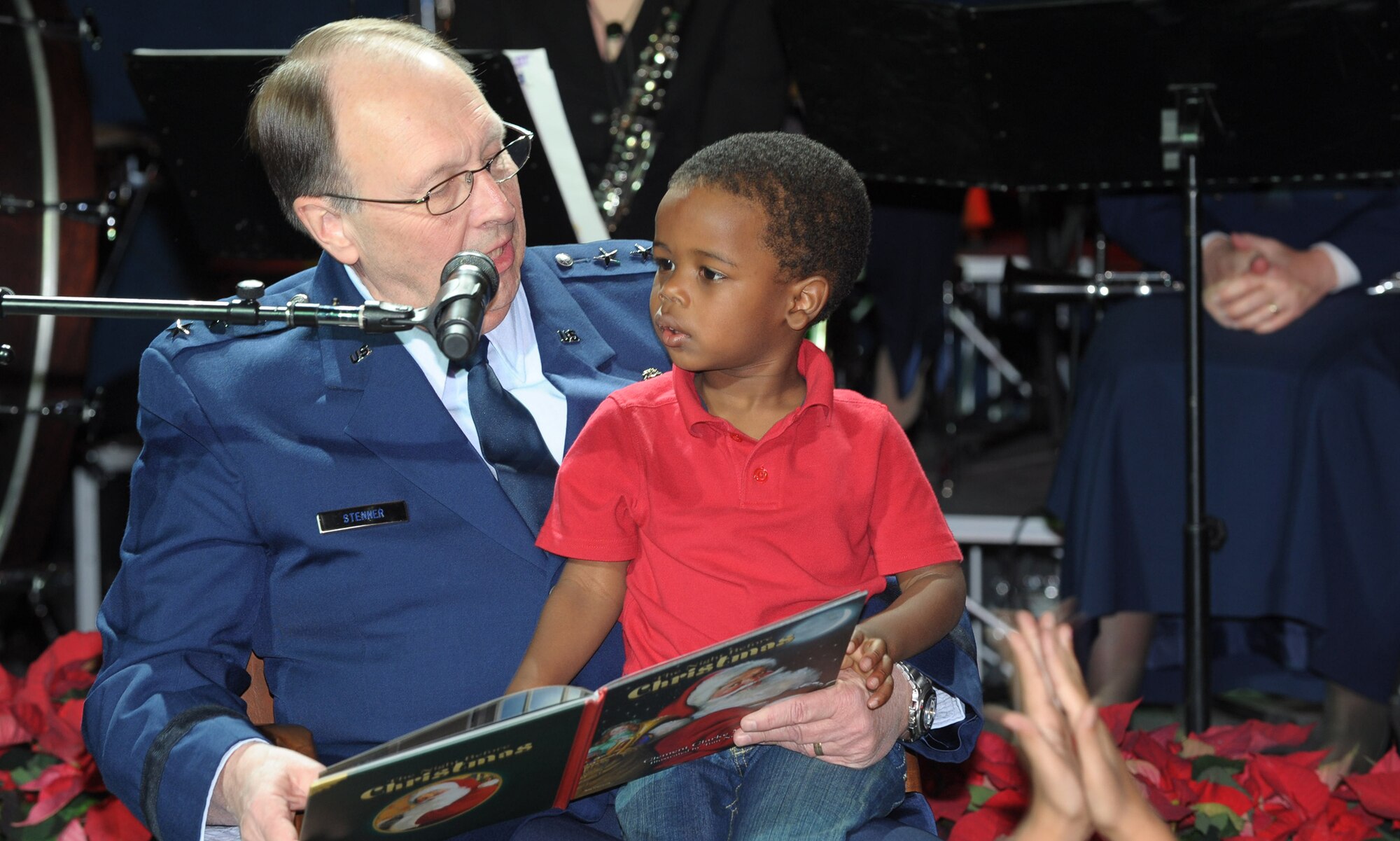 Cole Carter, son of Tech Sgt Edric and Senior Airman Sarah Carter, has the best seat in the house to listen to Lt. Gen. Charles E. Stenner, Jr., commander of Air Force Reserve Command, read "The Night Before Christmas" to children gathered at the annual Holiday Concert at the Museum of Aviation at Robins Air Force Base, Ga., Dec. 9, 2010. The Band of the U.S. Air Force Reserve performed for more than 800 members of the Warner Robins community who attended the event. (U.S. Air Force photo/Ray Crayton)
