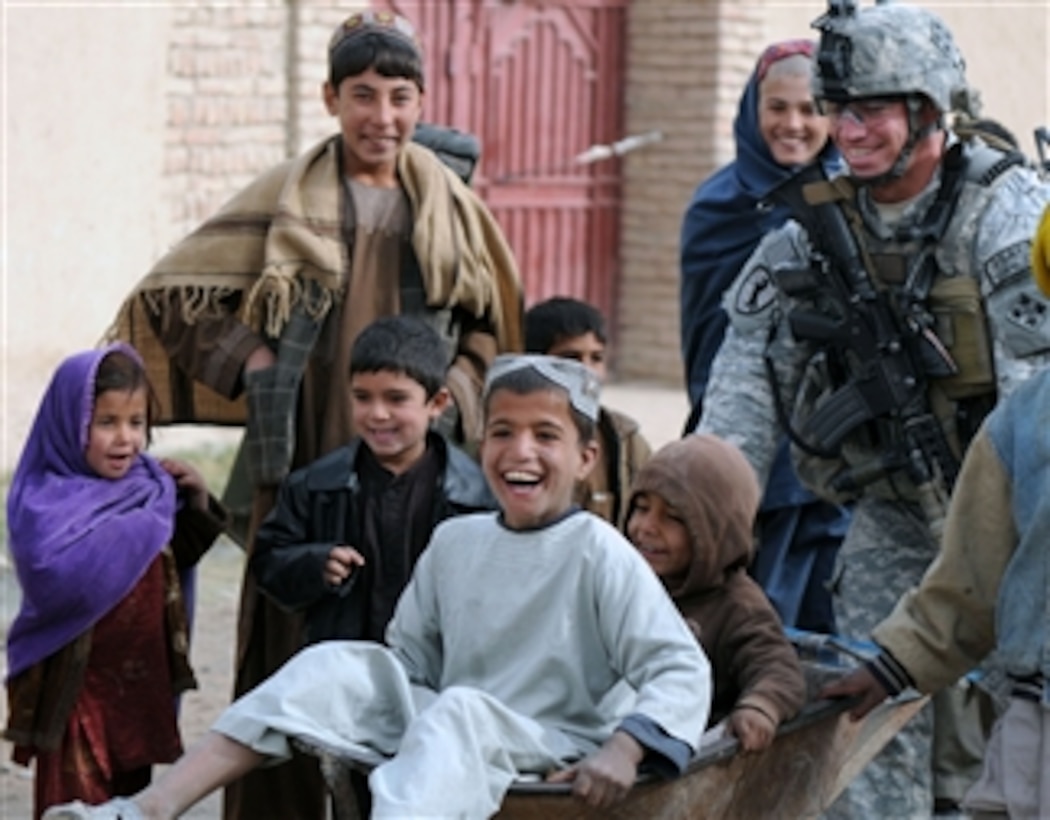 U.S. Army Staff Sgt. Kenneth Bower with Charlie Company, 1st Special Troops Battalion, 1st Brigade Combat Team, 4th Infantry Division pushes children in a wheelbarrow during a foot patrol through Kandahar City's Popal colony in Kandahar province, Afghanistan, on Dec. 5, 2010.  
