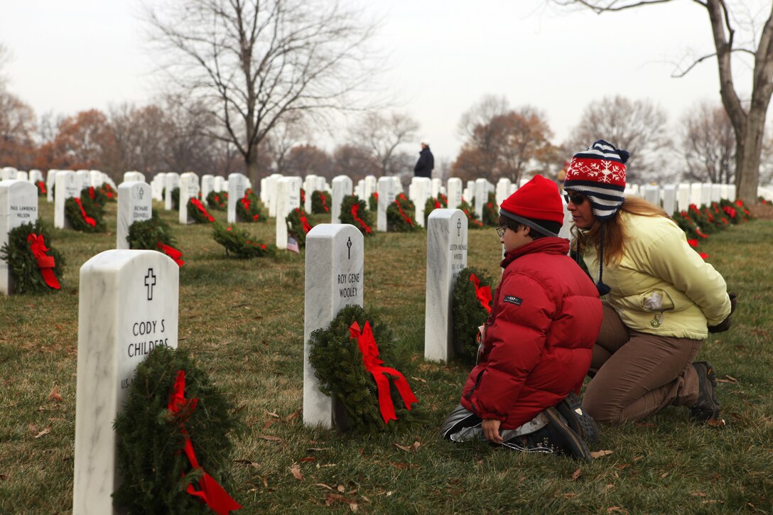 A young boy and his mother pay their respects to the headstone of a fallen service member during a wreath laying ceremony at the Arlington, National Cemetery, Dec. 11. This family was one of thousands in attendance who helped lay a total of 24,000 wreaths, ensuring that those who gave the ultimate sacrifice in times of war are not forgotten during the holidays.