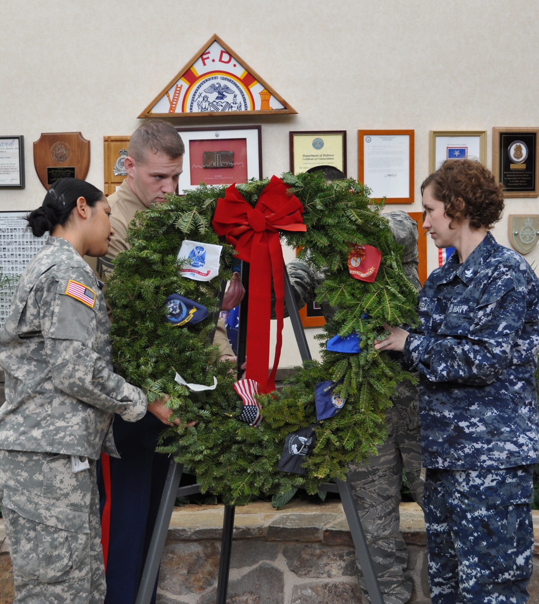 Army Sgt. Mariangelica Aviles (left) and Navy Petty Officer 2nd Class Jennifer Howell (right) assist Marine Cpl. Matthew Duerr and Air Force Airman 1st Class Vincent Montoya in placing the wreath on display in the Air Force Mortuary Affairs Operations atrium Dec. 11, 2010. The representation of each service was to honor all fallen military members during the Wreaths Across America ceremony held here. (U.S. Air Force photo/Christin Michaud)