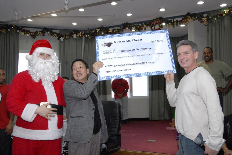 KUNSAN AIR BASE, Republic of Korea -- Tech. Sgt. Peter Rollins (left), 8th Fighter Wing Equal Opportunity office and Santa Claus, and Chaplain (Maj.) Timothy Porter (right), 8th Fighter Wing chaplain, present a check to the Mr. David Kim (center), director of the Il Mag Won orphanage Dec. 11.  The base chapel collected and donated over $3,000 on behalf of the wing for the orphanage, which will be used to purchase a water filteration system.  (U.S. Air Force photo/Capt. Sheryll Klinkel)
