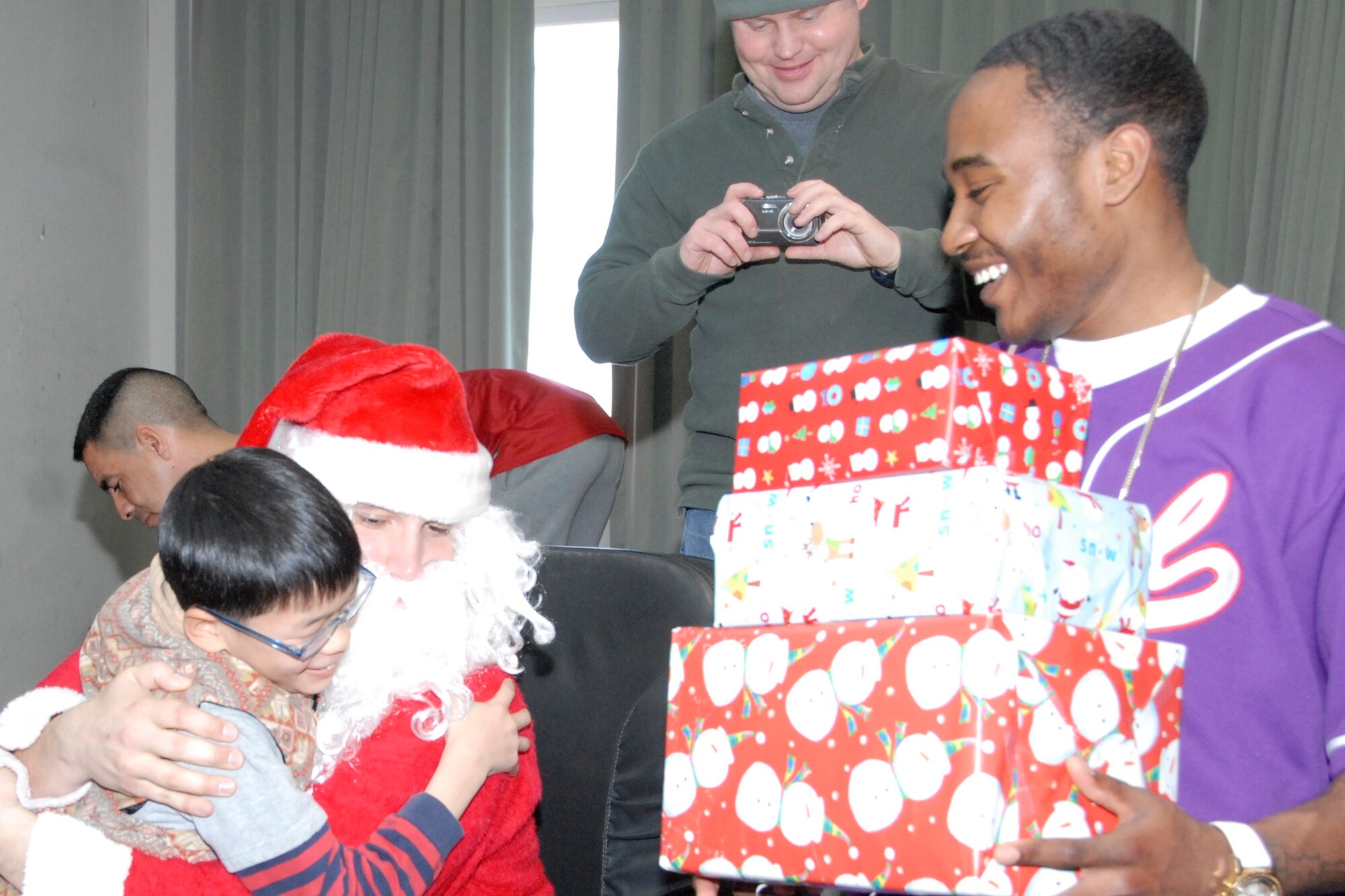 KUNSAN AIR BASE, Republic of Korea -- Tech. Sgt. Peter Rollins (left), 8th Fighter Wing Equal Opportunity office and Santa Claus, receives a huge from a child at the Il Mag Won orphanage Dec. 11 while Senior Airman Jeremy Bernard (right) gathers the child's presents.  Volunteers from the base chapel coordinated a holiday party for the children at the orphanage, where volunteers donated time, gifts, food and more to the children to celebrate the holiday season.  (U.S. Air Force photo/Capt. Sheryll Klinkel)