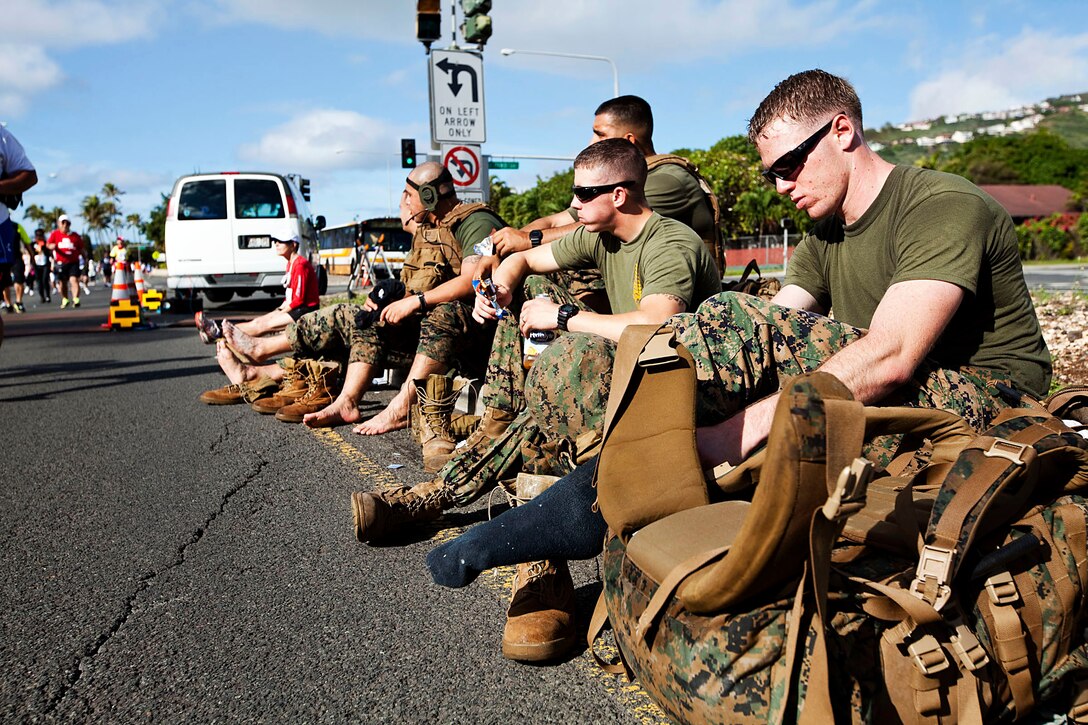 At right, Cpl. Brian Flannery, a firefighter with Aircraft Rescue Firefighting, Marine Corps Air Station Kaneohe Bay, Hawaii, and seven other Marines replenish their energy at the halfway point of the 2010 Honolulu Marathon, Dec. 12, 2010. For the second year in a row, the Marines hiked the 26.3-mile marathon with boots, camouflage trousers and 65-pound packs to raise money for wounded Marines and sailors at Wounded Warrior Battalion West — Detachment Hawaii, on Marine Corps Base Hawaii.