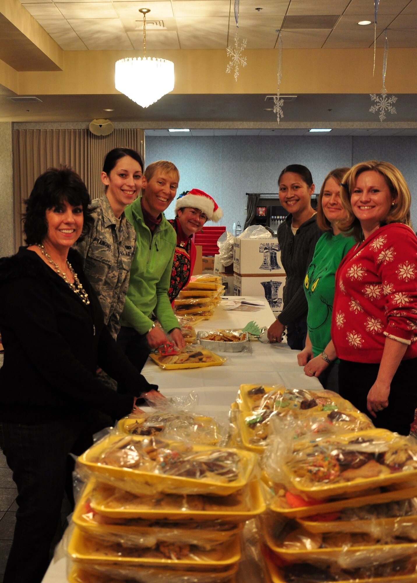Ana Alston, Airman 1st Class Sarah Tanguay, 90th Security Forces Squadron, Jill Miller, Anita Martinez, Minerva Maynard, Lissa Adams and Julie Tims pose for a photo in the Trail’s End Club Dec. 6 with some of the 500 trays of cookies volunteers put together for Airmen living in the dorms here. (U.S. Air Force photo by 2nd Lt. Stacey Fenton)