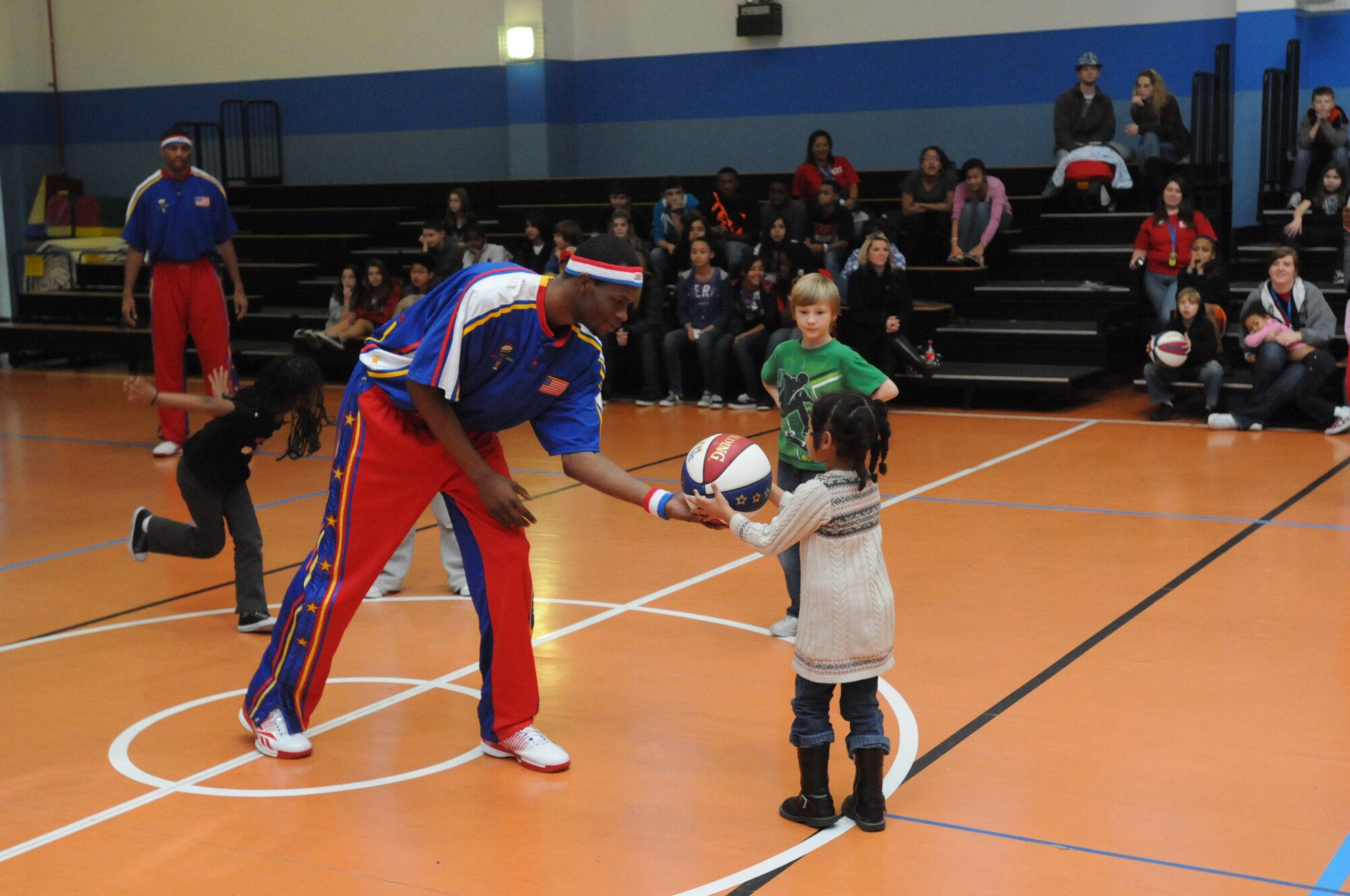 Harlem Globetrotter forward "Thunder" Petway assists an Aviano youth in performing a trick at the Aviano Youth Center Dec. 3 as part of the Globetrotter University program. The program aims to inspire youth to stay active by doing sports.(U.S. Air Force photo/Airman 1st Class LaVel Sterling)