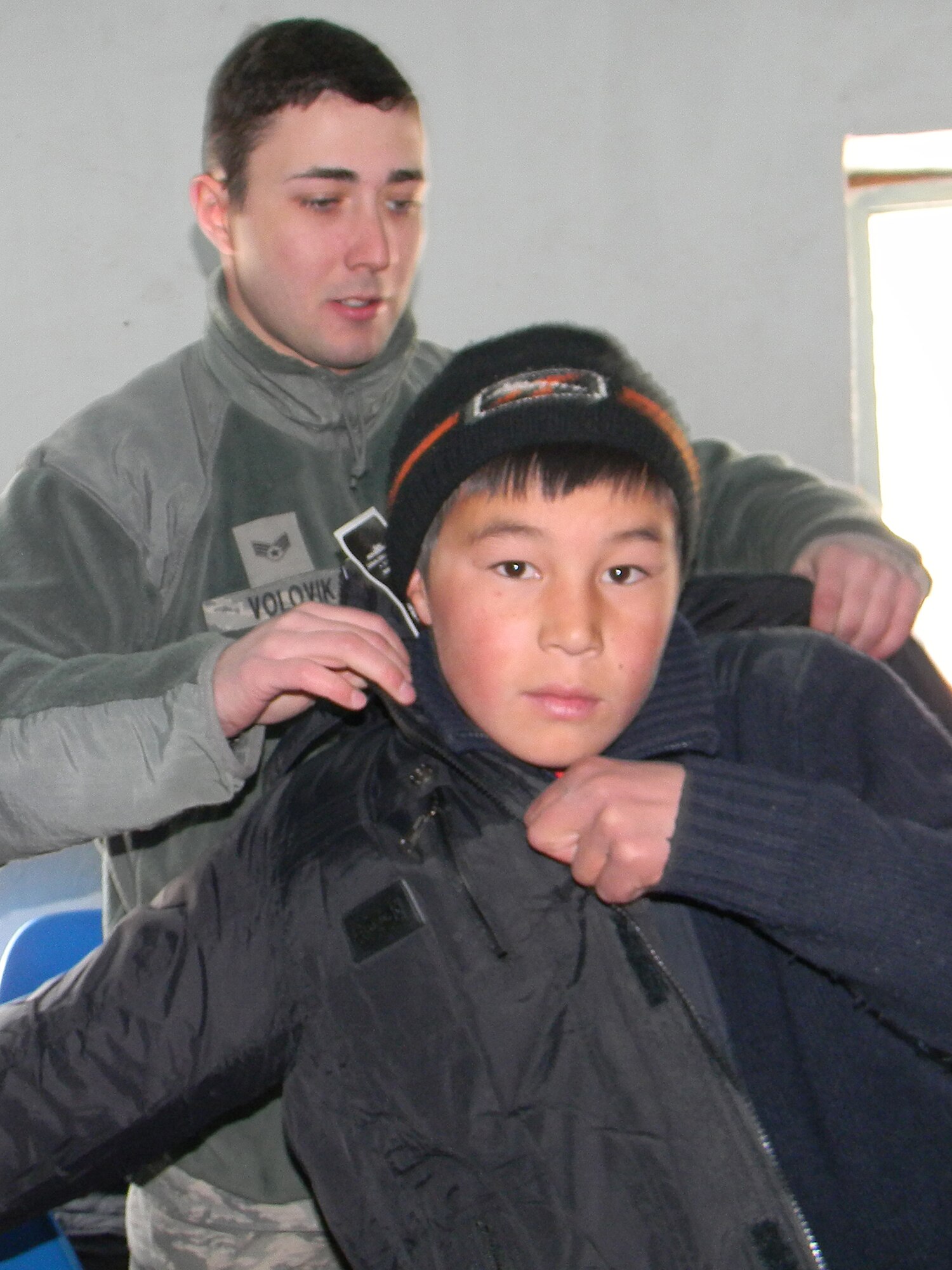 OSH, Kyrgyzstan - Senior Airman Ilya Volovik, Transit Center at Manas linguist, helps a child fit a coat during humanitarian assistance project Operation Warm & Dry II Dec. 8.  Transit Center at Manas Airmen teamed up with U.S. Office of Military Cooperation, Joint Distribution Effort, Kyrgyz Ministry of Emergency Situations, Osh Rayon governmental leaders and the Kyrgyz police department to distribute 3,500 pounds of clothing, 1,000 coats and 1,000 blankets to Toguz-Bulak and Sary-Kungoi villages.  (U.S. Air Force photo/Senior Airman Jennifer Archambault)