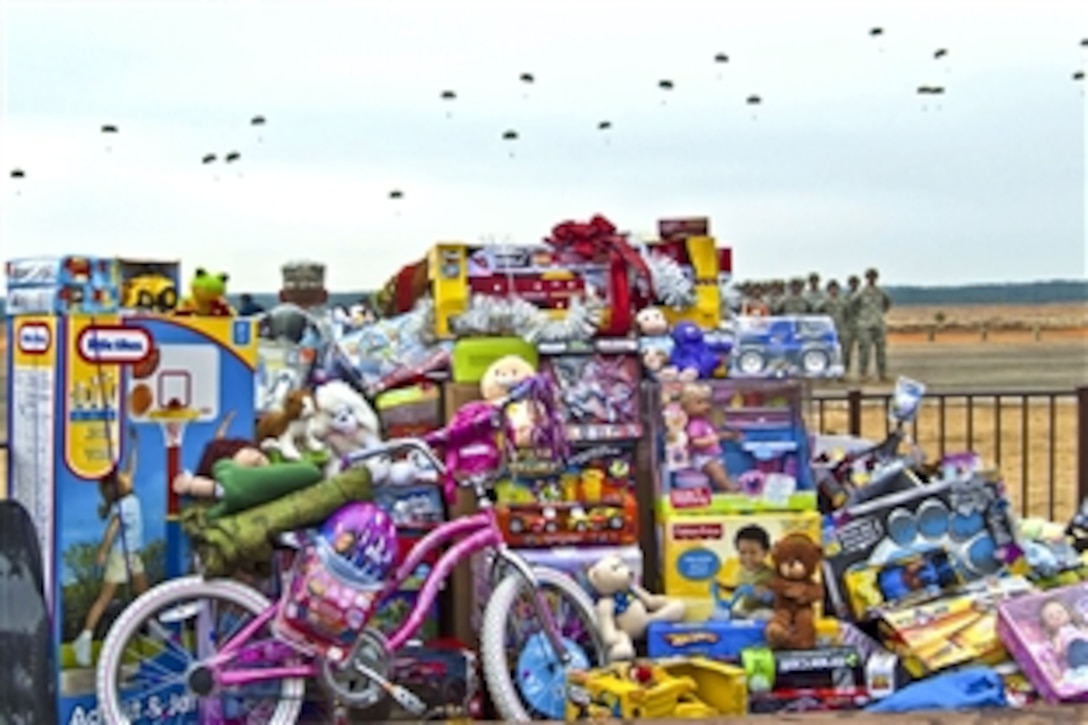 U.S. Army paratroopers fall from the sky behind a mound of donated toys at Sicily Drop Zone on Fort Bragg, N.C., Dec. 11, 2010. Paratroopers donated more than 5,000 toys to local children during Operation Toy Drop, hoping to brighten their holidays.