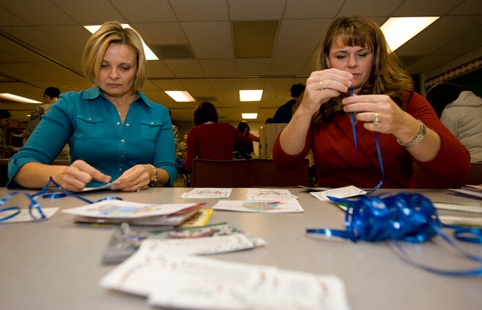 NELLIS AIR FORCE BASE, Nev. -- Karmen McCloud, wife of Lt. Col. Mark McCloud, 99th Civil Engineering Squadron commander, and Missy Cornish, wife of Col. Barry Cornish, 57th Wing vice commander, tie ribbons to cards made by local elementary school students in the Las Vegas area during the Annual Cookie Drive Dec. 14. The cookie drive is held during the holidays for single Airmen living in the dorms. (U.S. Air Force photo by Senior Airman Brett Clashman/Released)