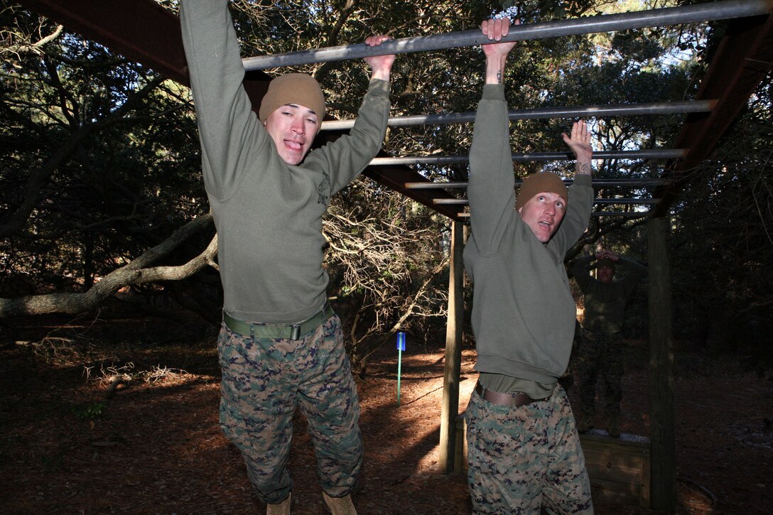 Staff Sgt. Joseph Cusimano, a native of Sulphur, La., and an ammunition technician at MCTAG, and Gunnery Sgt. John Jones, a native of Ft. Myers, FL. and supply chief at MCTAG, swing through the “Tarzan” monkey bars at the JEB Little Creek-Fort Story obstacle course, Wednesday.