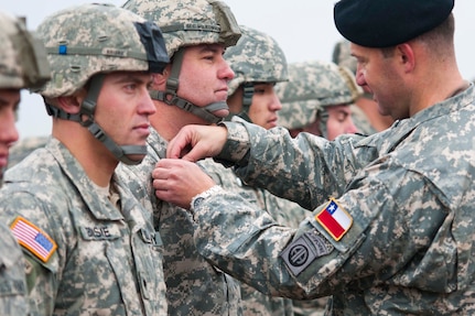 A Chilian jumpmaster pins on jump wings from his country on a U.S. paratrooper during the rain and cold at Operation Toy Drop on Sicily Drop Zone, Dec. 11. Wings are obtained when a U.S. military service member conducts multi-national airborne operations with a foreign-service jumpmaster. (U.S. Army photo/Sharilyn Wells)