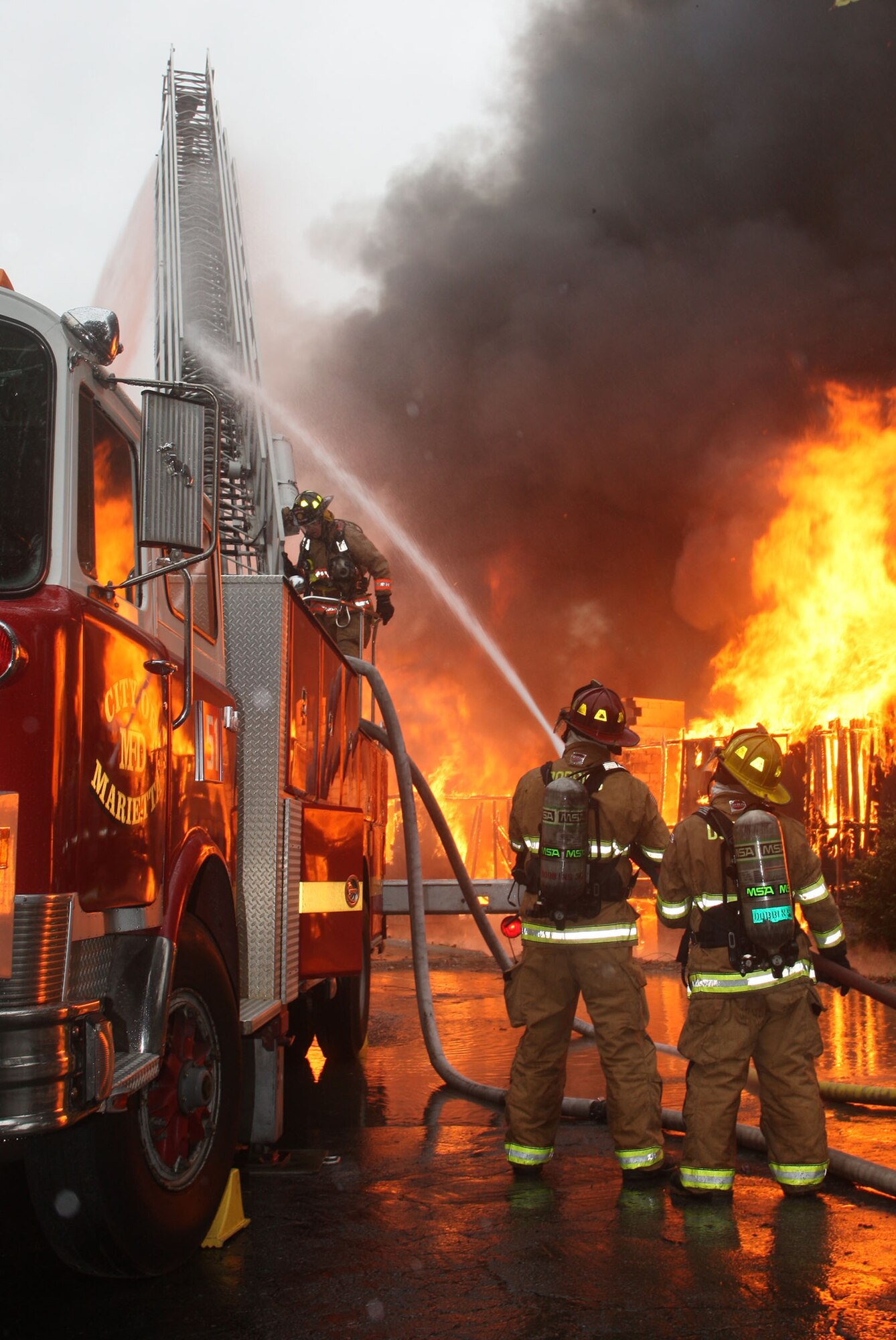 Firefighters from Dobbins Fire and Emergency Services Team assist local firefighters by spraying down the ladder as the intense heat from the blaze makes it difficult to climb. (U.S. Air Force Photo/Don Peek) 