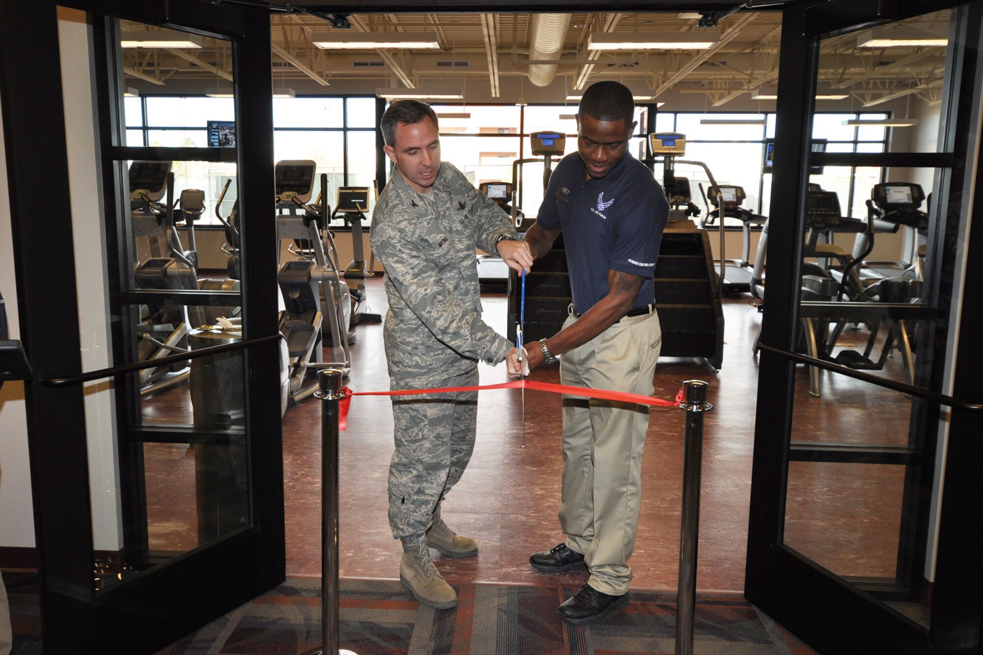 PETERSON AIR FORCE BASE, Colo. -- Col. Stephen N. Whiting (left), 21st Space Wing commander, and Airman 1st Class Keith Proctor, 21st Force Support Squadron fitness apprentice, cut the ribbon Dec. 10 at the Peterson Sports and Fitness Center’s new 2,700 square-foot cardio room. The room features 30 state-of-the-art cardio machines, including six Arc trainers that combine elements of climbing, hiking and skiing for low impact cardio. All of the machines are iPod accessible and the room also features two large televisions. The $788,000 cardio room, including equipment, is the first phase of adding more gym space to Peterson AFB, where an estimated 2,500 people use the gym every day. (U.S. Air Force photo/Jennifer Brite)