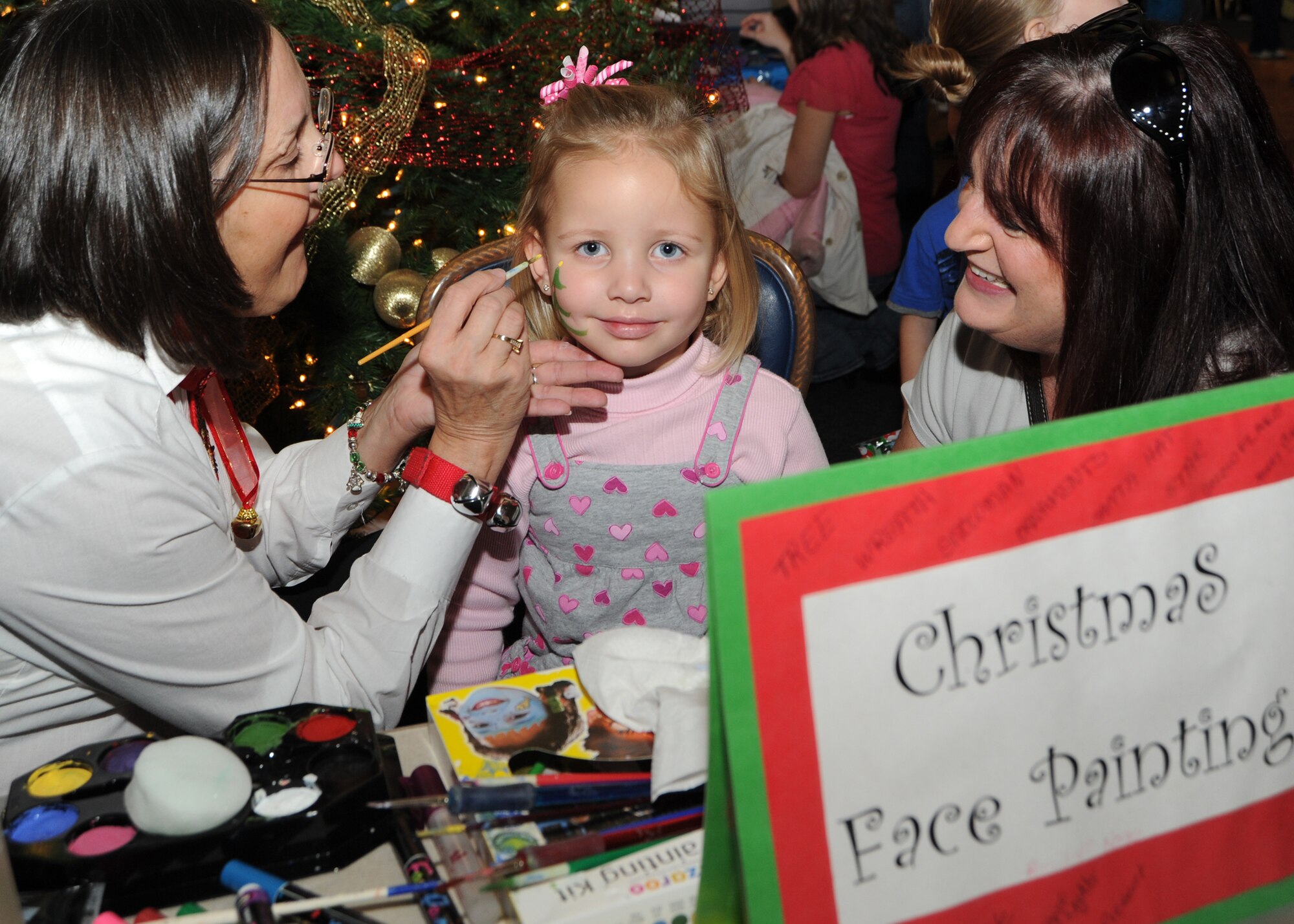 “Sonshine,” a clown from the Ambassador of Good Will Clowns, paints a Christmas tree on, 3-year-old Trinity Smith, while her grandmother Sandi Cairns watches, during Santa’s Visit Dec. 11, 2010, McConnell Air Force Base, Kan. Team McConnell members had the opportunity to spend time with family, take pictures with Santa, play free games, win prizes and participate in craft activities. (U.S. Air Force photo/Senior Airman Maria A. Ruiz)  