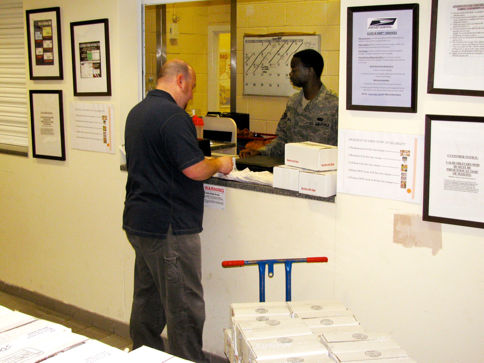 RAF MILDENHALL, England -- Micah Steinwandt, Single Airmen's Ministry director, does the paperwork to mail boxes containing Christmas stockings and small gifts to deployed single Airmen, as Staff Sgt. Juante Smith, 100th Communications Squadron Post Office, helps the process go smoothly with the large amount of packages being mailed. The gifts were donated by members from the RAF Mildenhall Chapel community. (U.S. Air Force photo/Staff Sgt. Melvin Adkins) 