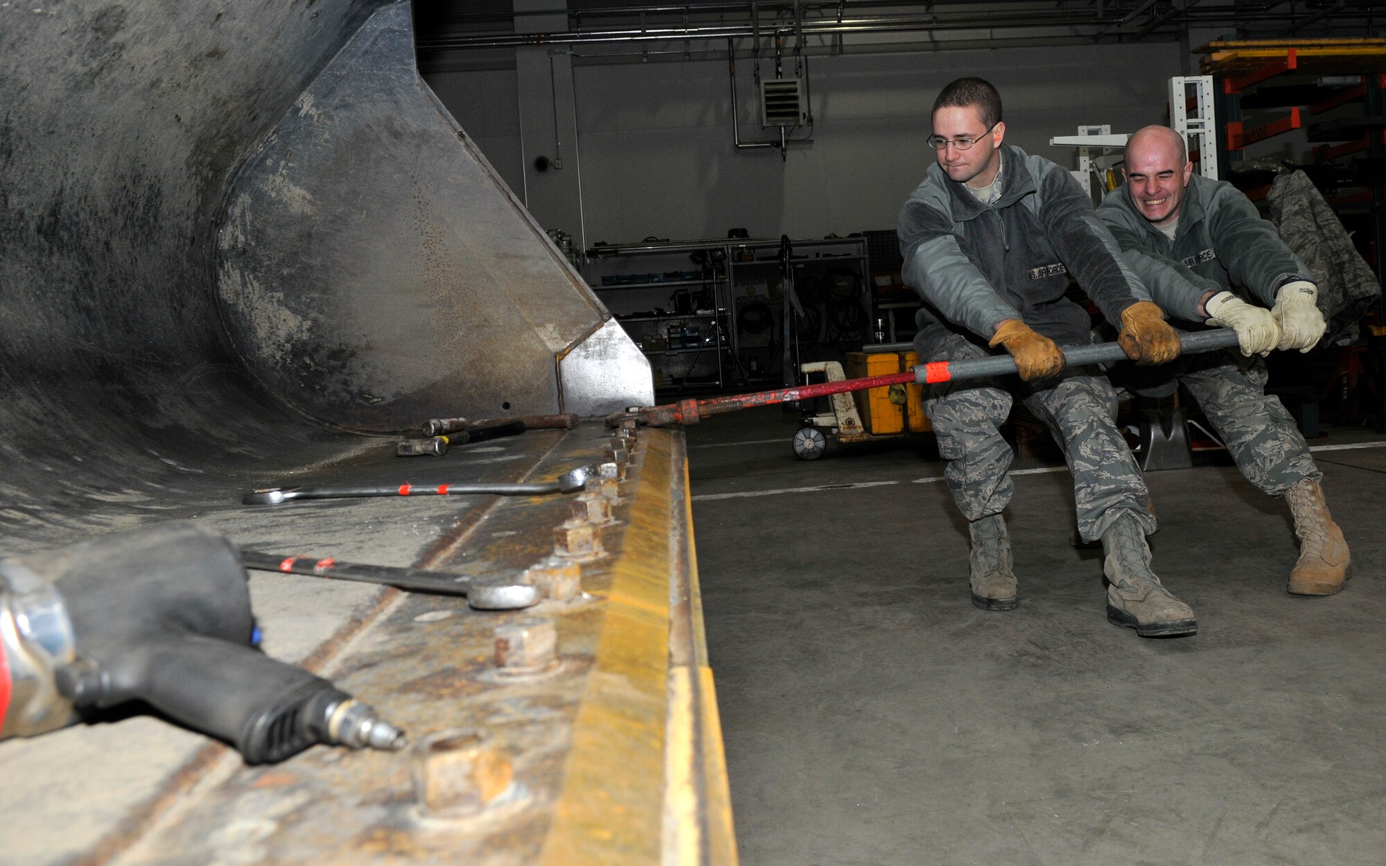From the left, U.S. Air Force Airman 1st Class Steven Leary and Tech. Sgt. Christopher Messmer, 35th Civil Engineer Squadron pavements and equipment construction technicians, strain on a cheater bar slid over a pipe wrench to loosen rusted bolts on a front-end loader’s bucket Dec. 16, 2010, Misawa Air Base, Japan. The front-end loader is equipped with sacrificial skid plates on the bucket, which take the abuse of grinding on the ground instead of the more expensive bucket. (U.S. Air Force photo by Tech. Sgt. Phillip Butterfield/Released)

