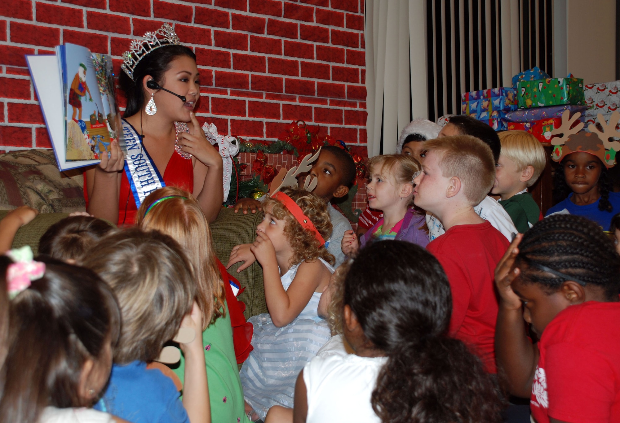 Children gather around as Cassie Sumimoto, Miss Teen South Pacific World 2011, reads a story during the Deployed Spouse's Christmas Party Dec. 14 at the Hickam Communities Center, Joint Base Pearl Harbor-Hickam, Hawaii. The 647th Air Base Group, with Warfighter Family Readiness Services, hosted the party. More than 55 families, including 111 children attended. Col. Rusty Baumgardner, 647 ABG commander and JBPH-H deputy commander, and many other key leaders provided entertainment and support for families in attendance. The evening concluded with a visit from Santa Clause who provided a present to each of the good boys and girls at the party. (U.S. Air Force photo/Tech. Sgt. Anthony O'Brien)