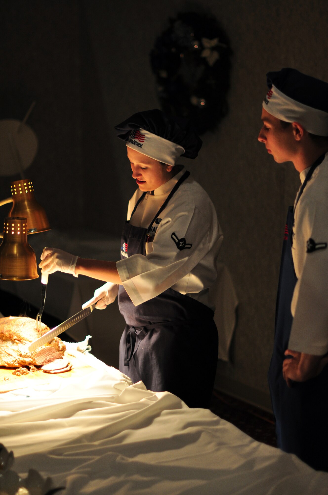 Airmen Kaitlyn Watson and Joshua Herrington, both 90th Forces Support Squadron, serve members of the Mighty Ninety serve ham during the wing holiday party held in the Trail’s End Club on Dec. 11. (U.S. Air Force photo by Staff Sgt. Chad Thompson)