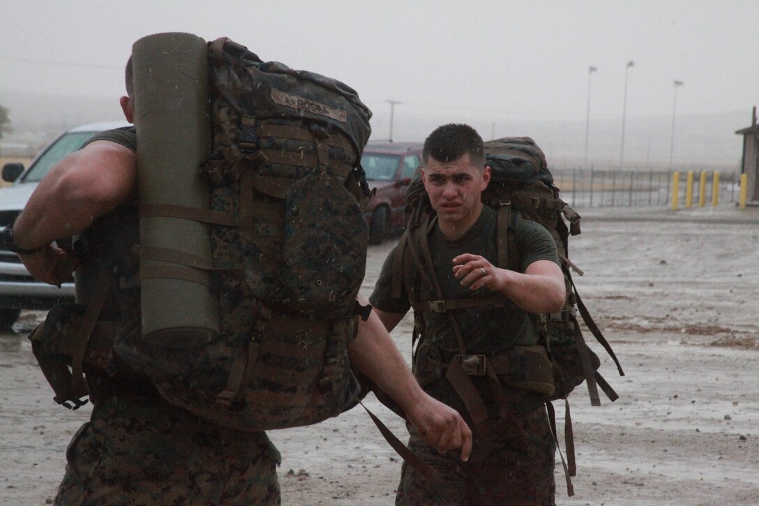 A Combat Center Marine prepares to hand off his pack so he can fireman carry a Marine during rain-soaked physical training Dec. 21, aboard the Corps’ premiere combined-arms, live-fire training facility located in the Mojave Desert.
