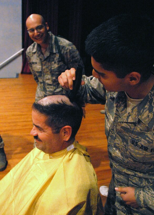 Chief Master Sgt. John Trujillo (left) gets his head shaved Dec. 17at the 383rd Training Squadron final formation in the Base Theater. Chief Trujillo, 383rd TRS superintendant, made a bargain with the Airmen at a final form if they went from 45 to 60 days with zero alcohol-related incidents, he would shave his head. Airman 1st Class James Qureshi and Airman Jonathon Dominguez were picked to shave the chief’s head after their class won the 383rd TRS class canned food drive competition. (U.S. Air Force photo/Mike Litteken)  